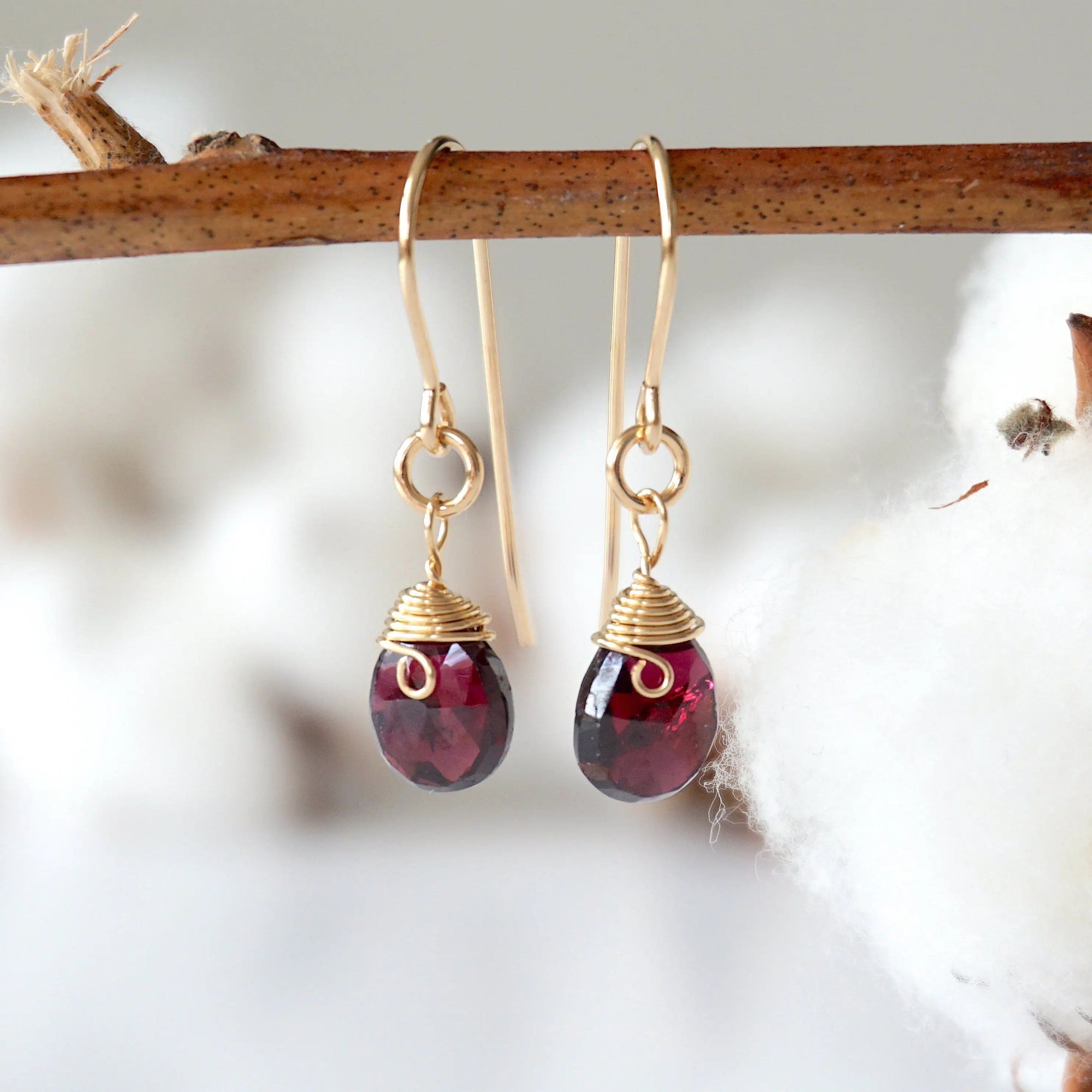 Front view of faceted garnet 14k gold filled drop earrings on display stand, handmade January birthstone dangle earrings