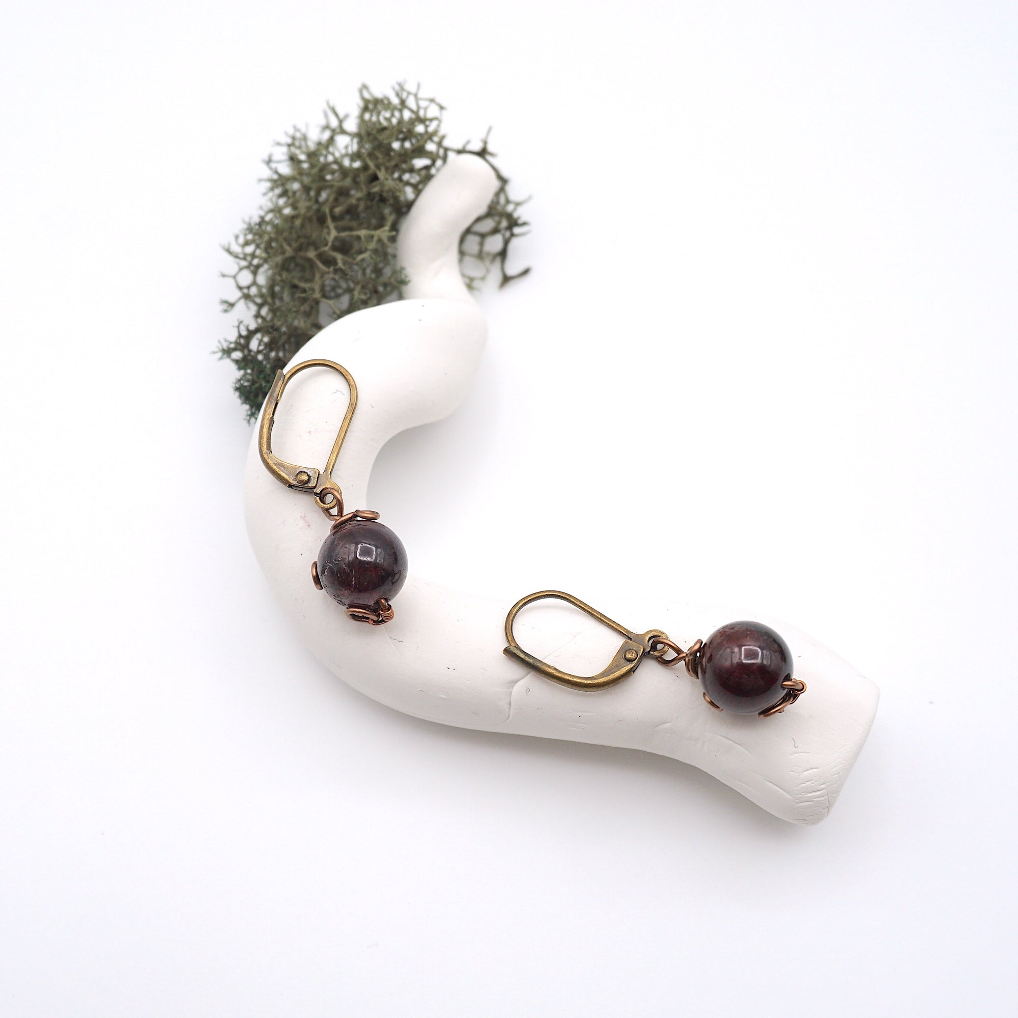 Bird’s eye view of garnet drop earrings laying flat on a display, showing detailed wire wrapping and gemstone color.