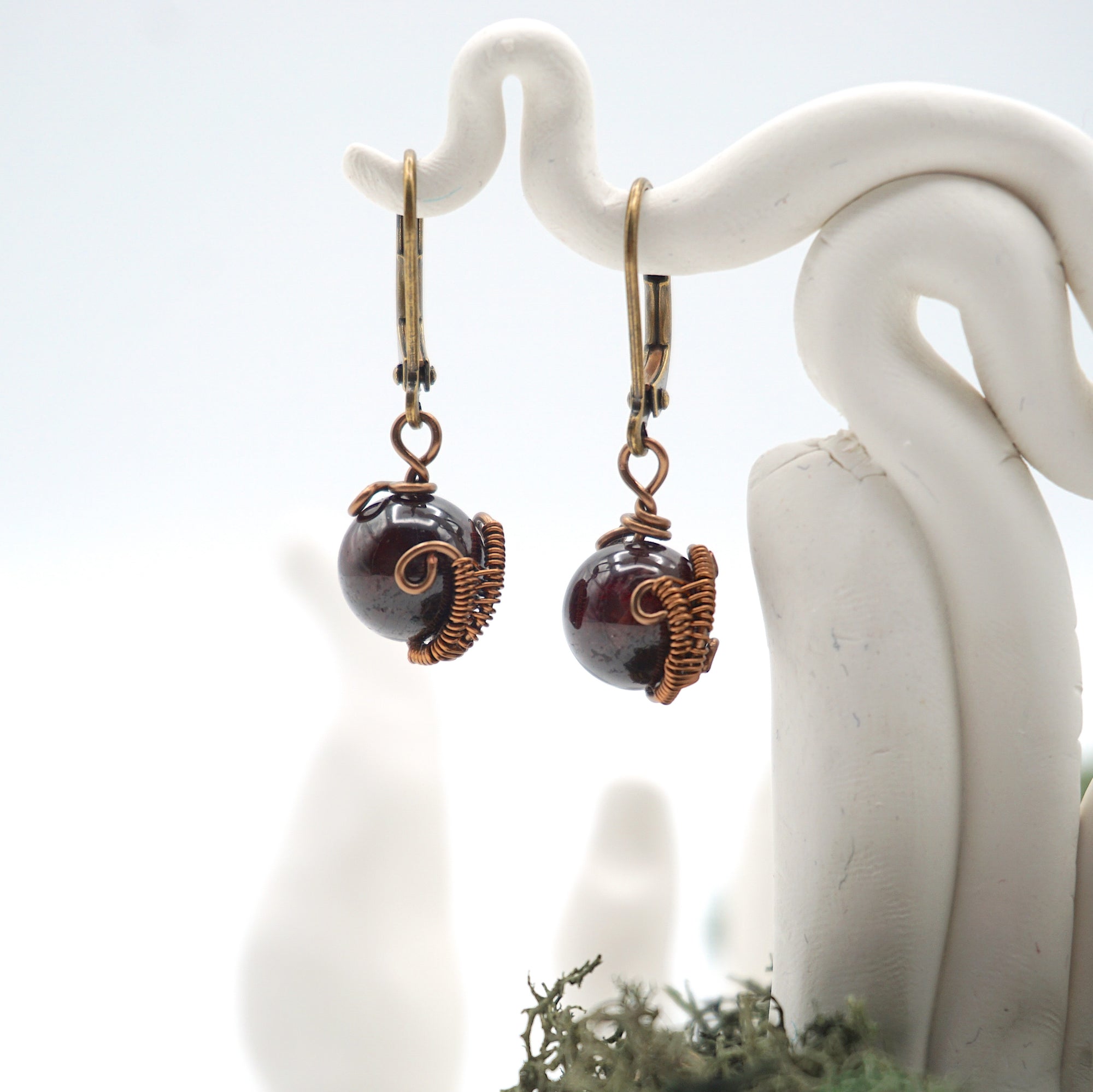Close-up view of handcrafted natural garnet drop earrings with antique bronze copper wire wrapping.