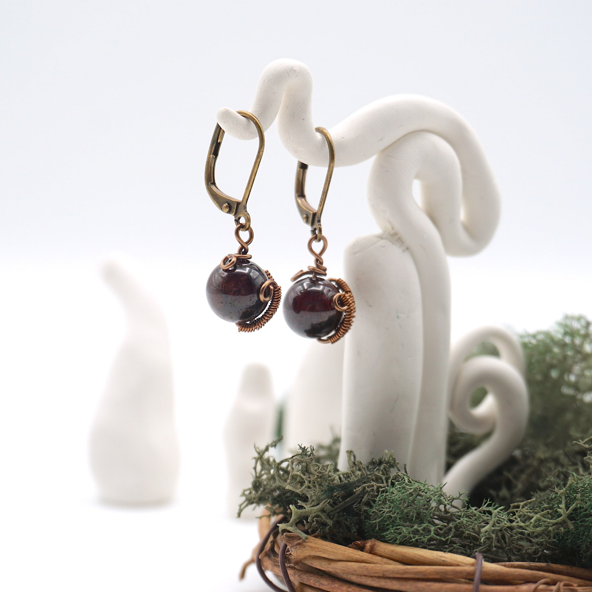 Side angle of garnet drop earrings on a display stand, highlighting antique bronze copper wire wrapping.