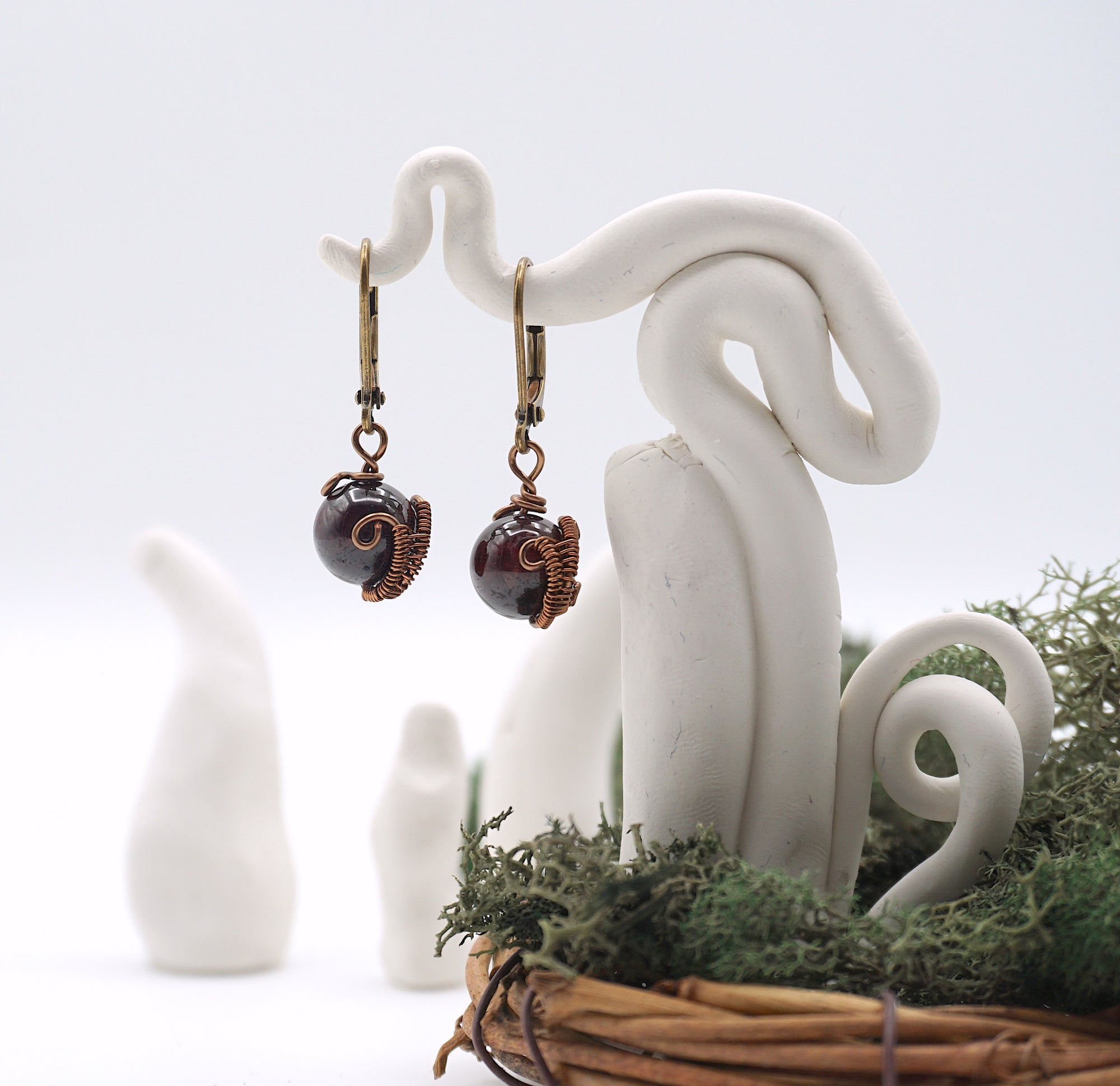 Front angle of garnet drop earrings hanging on a jewelry display, showcasing wire-wrapped design.