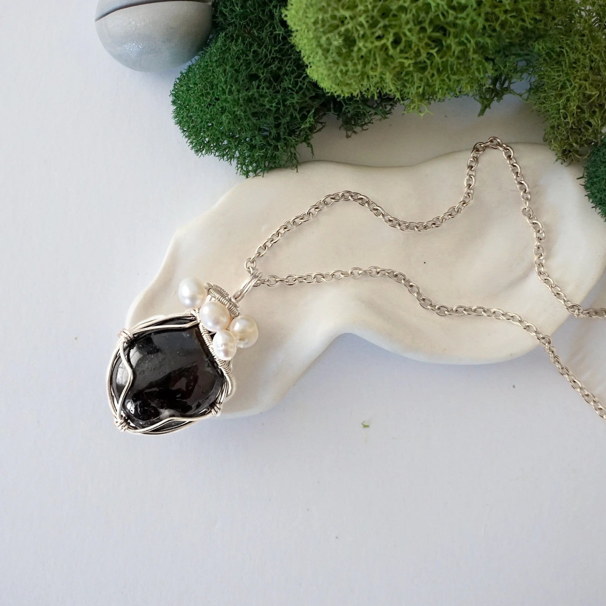 Handmade silver wire wrapped garnet and freshwater pearl necklace laying flat on a silver plated chain, artisan jewelry for women