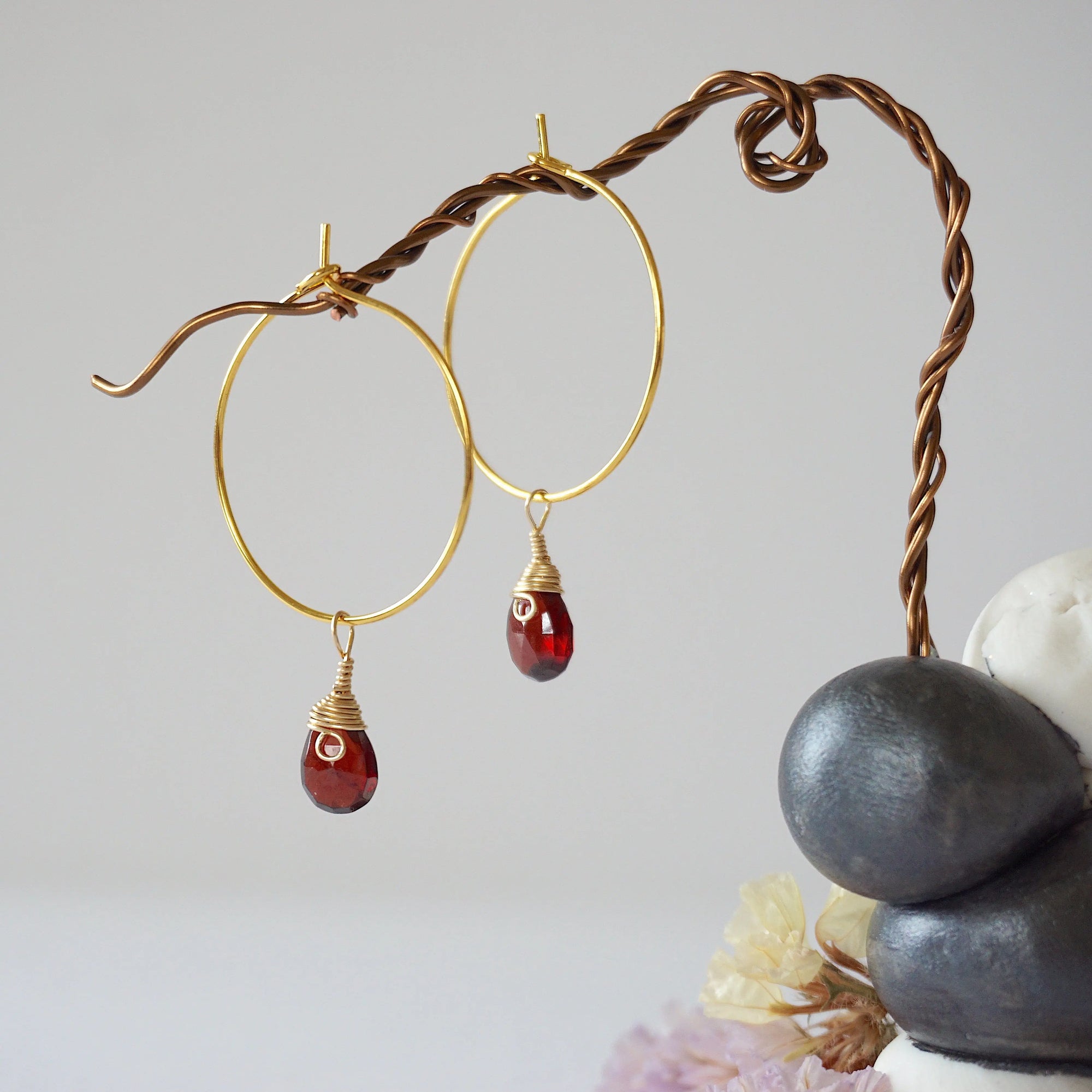 Close-up of handcrafted garnet hoop drop earrings in gold plated brass, featuring wire wrapped natural red garnet gemstones on a jewelry display