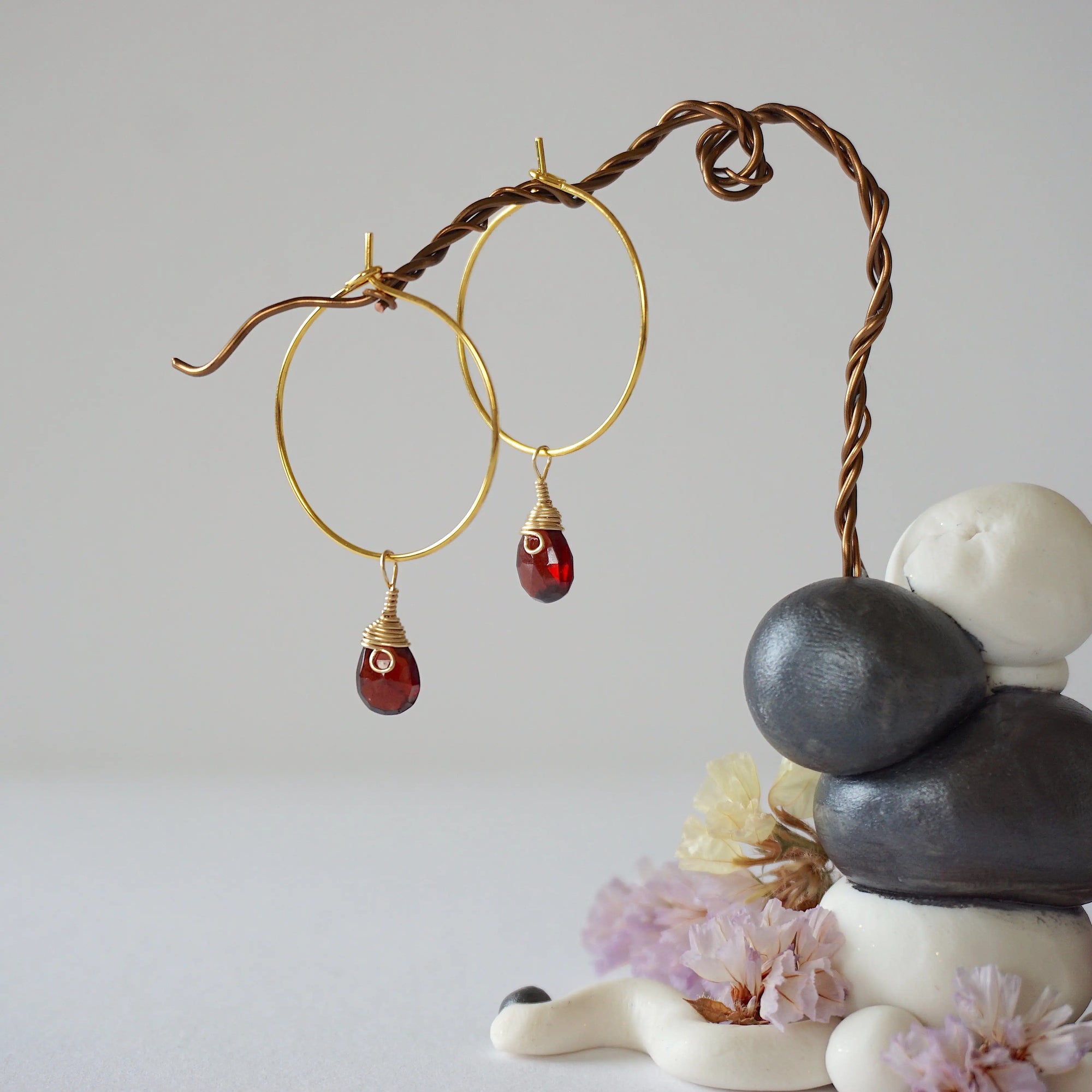 Angled view of gold plated garnet hoop earrings with wire wrapped gemstone drops, showing faceted January birthstone detail