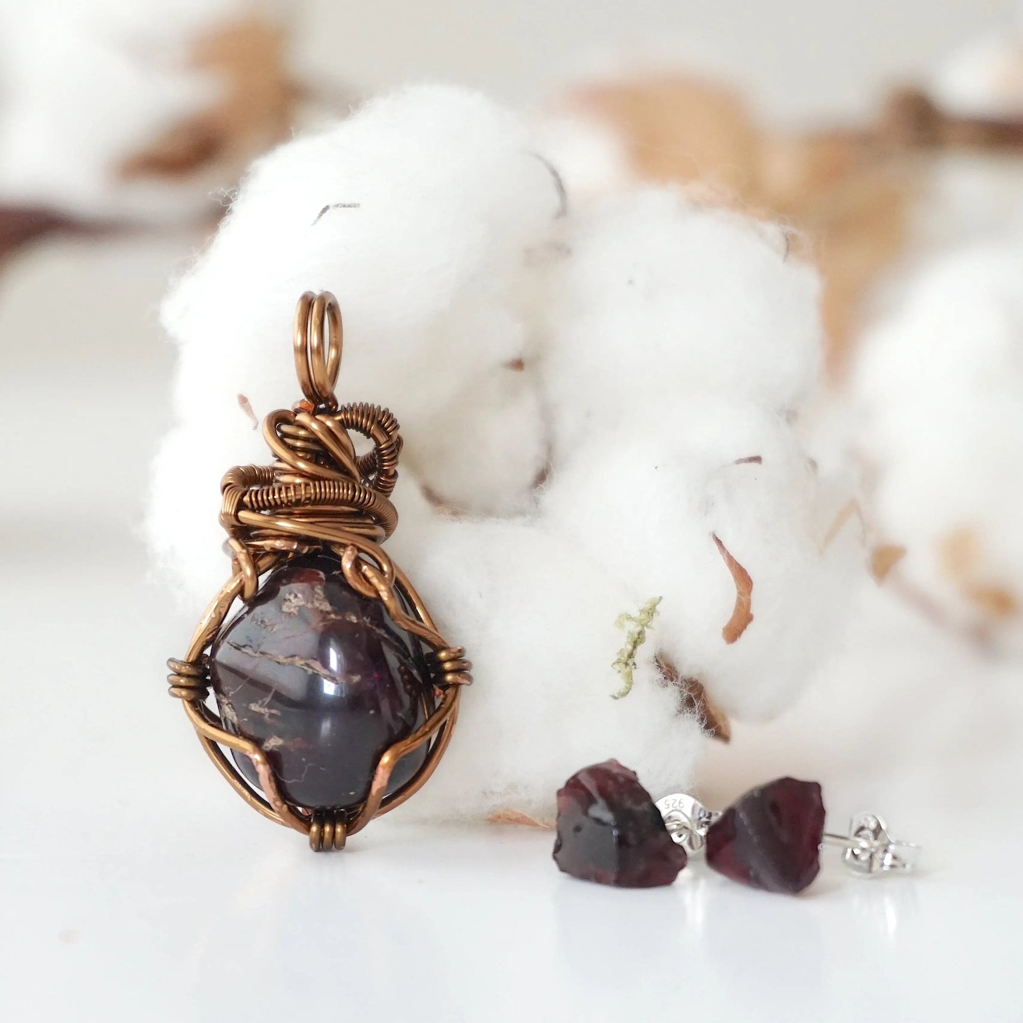 Back view of a wire wrapped garnet pendant and side view of garnet stud earrings in a women’s jewelry set