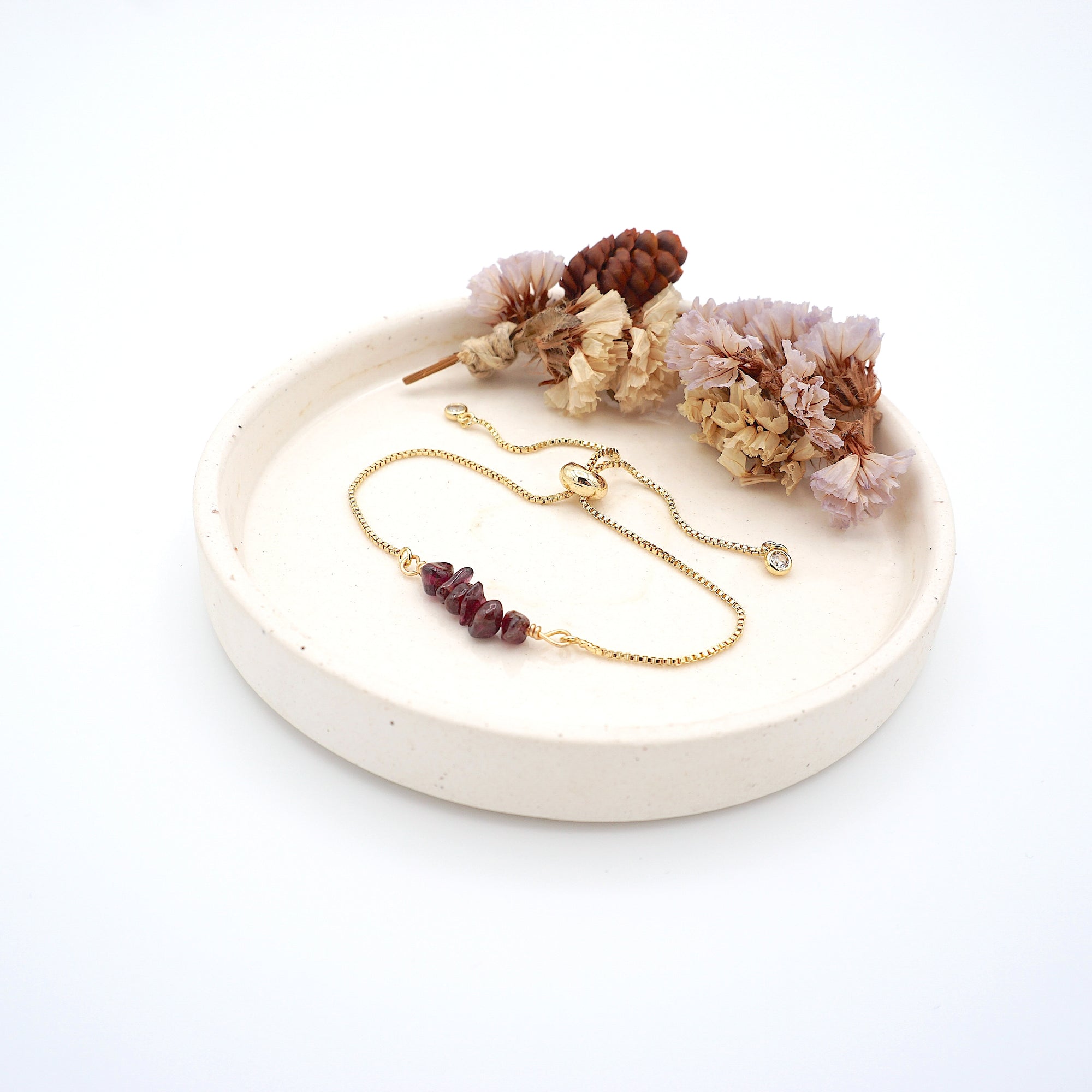 Handmade garnet bracelet displayed on ceramic tray showing natural red crystals and gold chain - January birthstone gift for her