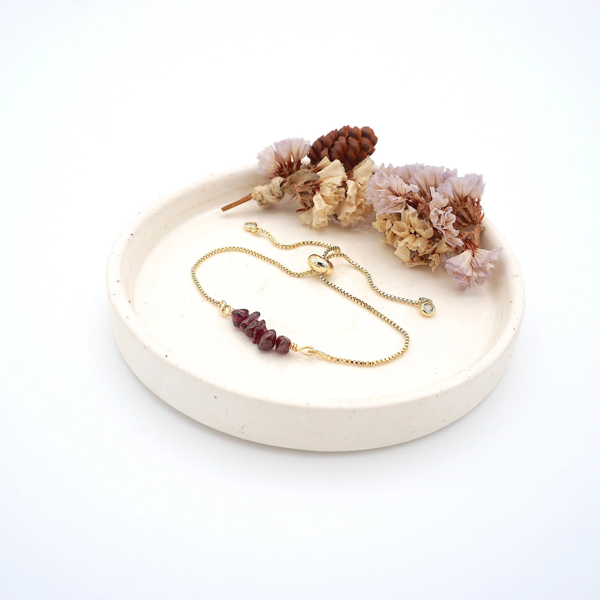 Handmade garnet bracelet displayed on ceramic tray showing natural red crystals and gold chain - January birthstone gift for her