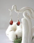 Detailed front view of handcrafted garnet sterling silver drop earrings with natural faceted garnet, artisan wire wrapping, hanging from a display – Designs by Nature Gems