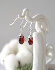 Side view of sterling silver garnet drop earrings showing wire wrapped natural faceted garnet, artisan craftsmanship, on a display – Designs by Nature Gems