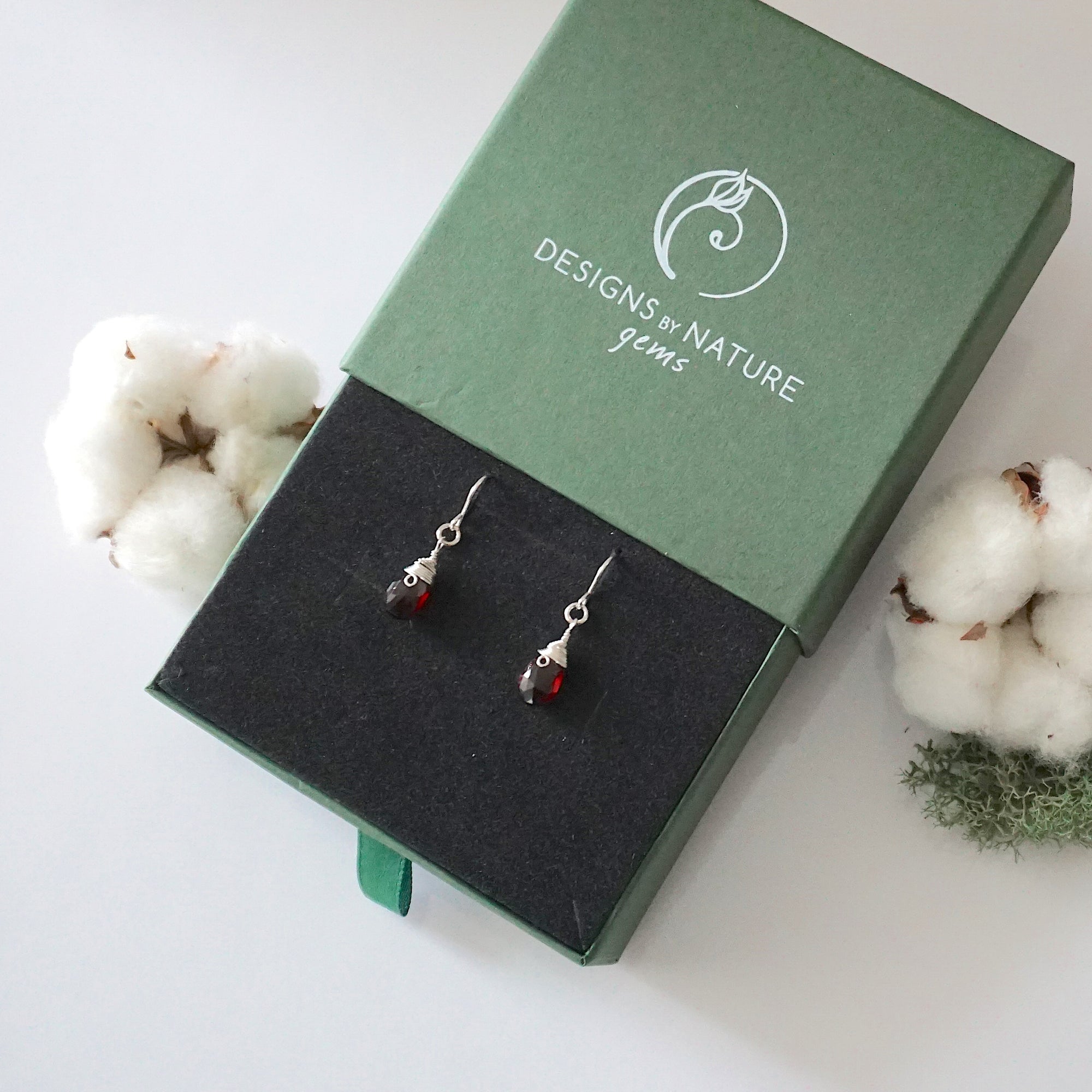 Garnet sterling silver drop earrings in branded Designs by Nature Gems jewelry box, showcasing handcrafted faceted garnet and sterling silver wire wrapping