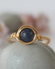 Front-angle detail of gold wire-wrapped sapphire ring showing the classic minimalist artisan setting for women