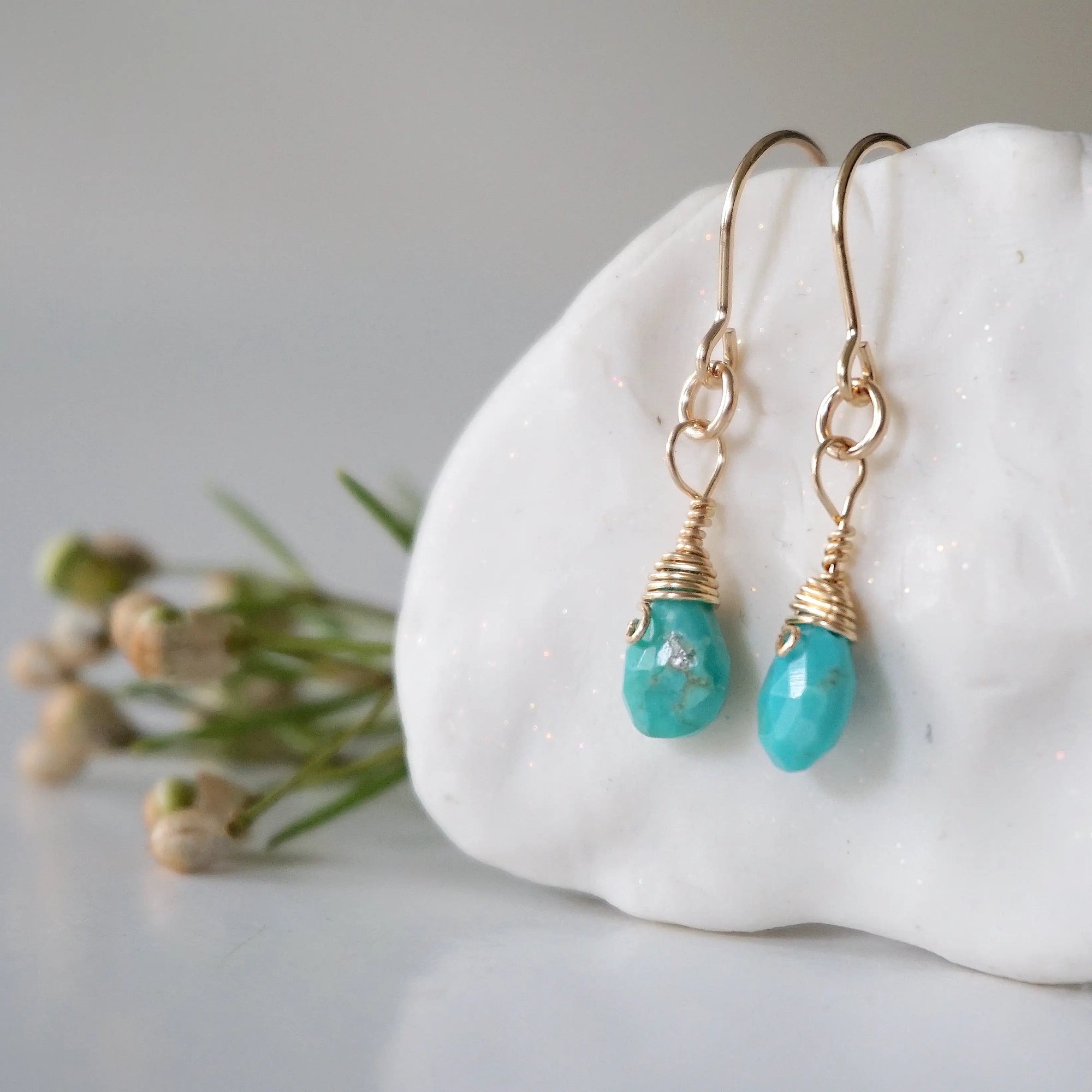 Left side angle of gold turquoise dangle earrings displaying handmade wire wrapped design and natural stone variation