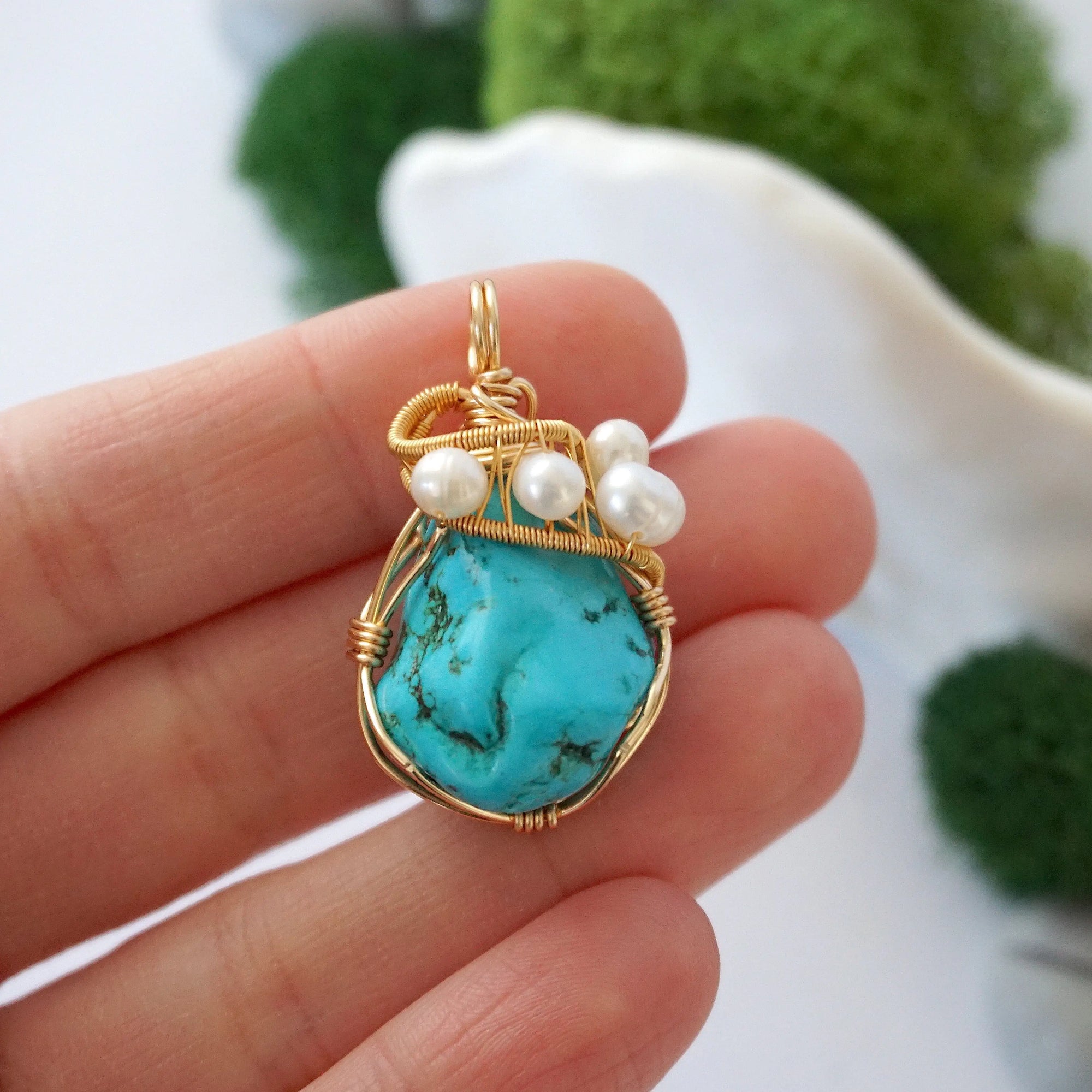 Turquoise and pearl pendant held in hand showing size of wire wrapped gold necklace for women