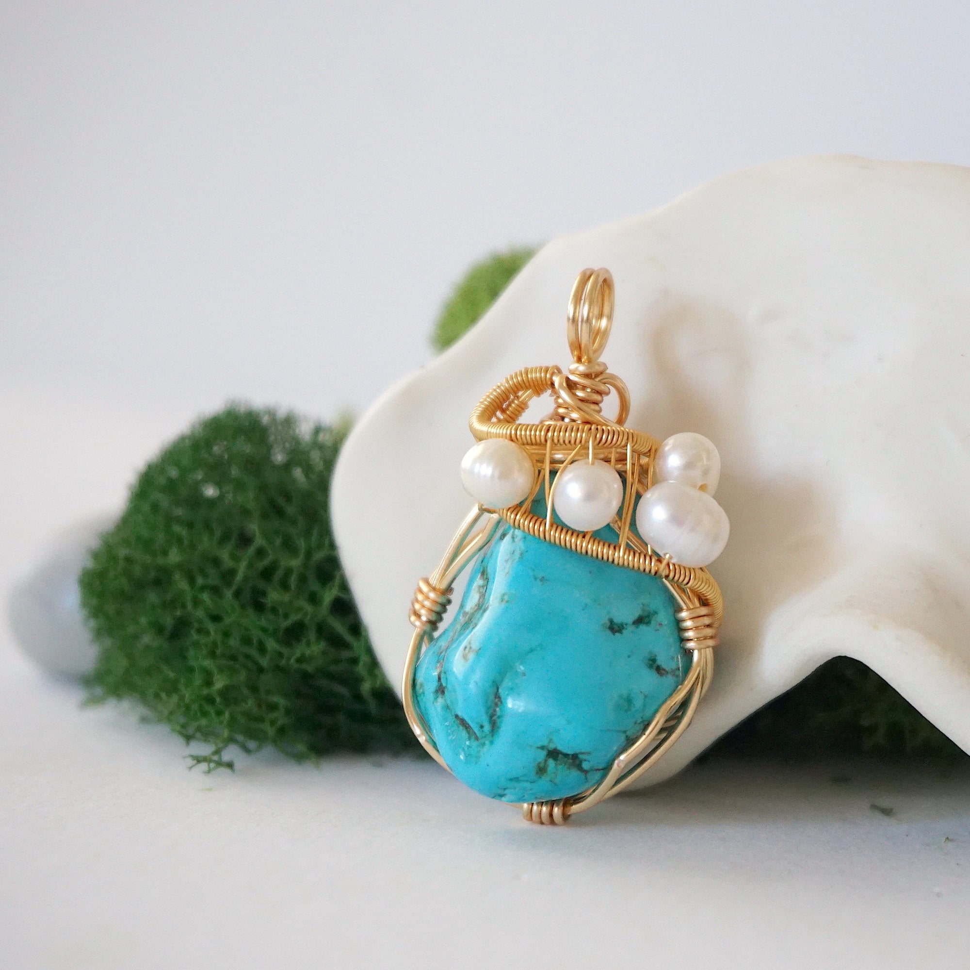 Side angle of raw turquoise and pearl pendant showing wire wrapping depth and natural crystal texture