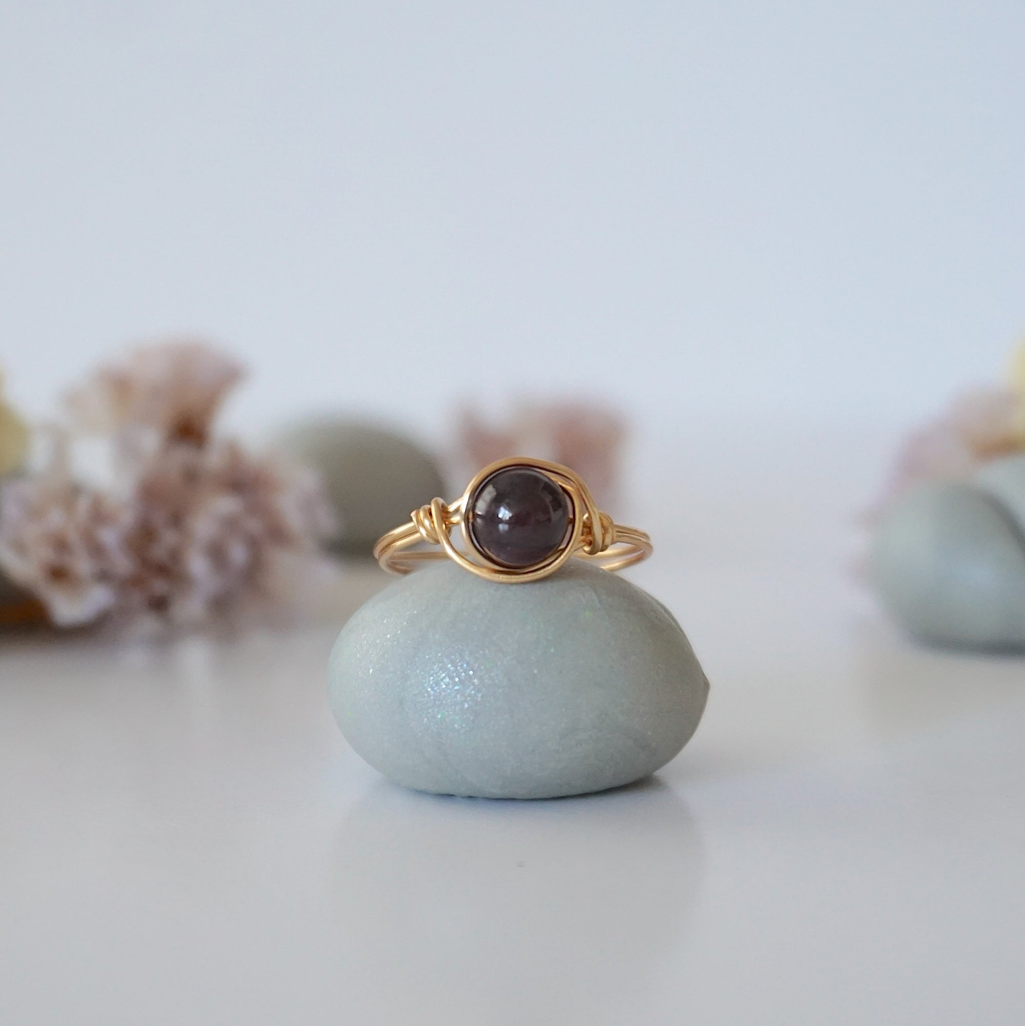 Front detail of simple garnet bead ring with minimalist gold wire wrapping on display