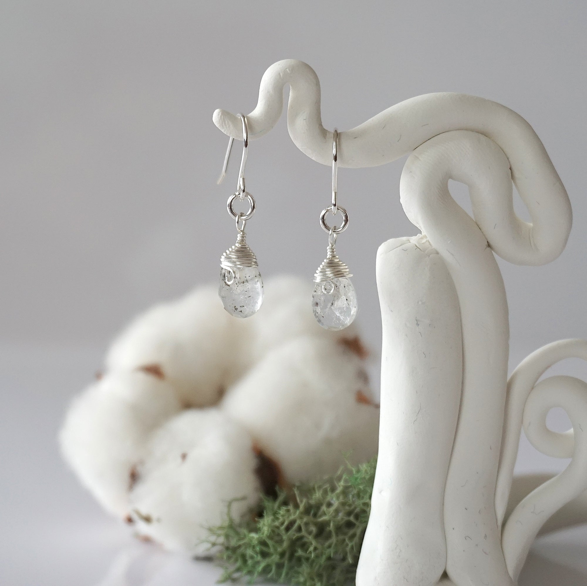 Detailed front view of handcrafted Herkimer diamond sterling silver drop earrings with natural faceted Herkimer diamond, artisan wire wrapping, hanging from a display – Designs by Nature Gems