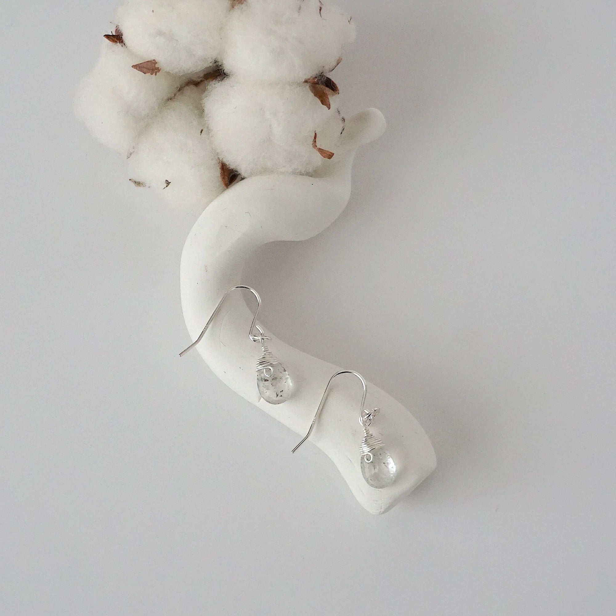 Herkimer diamond sterling silver drop earrings with faceted natural Herkimer diamond stones and wire wrapping, laying flat on a display – Designs by Nature Gems