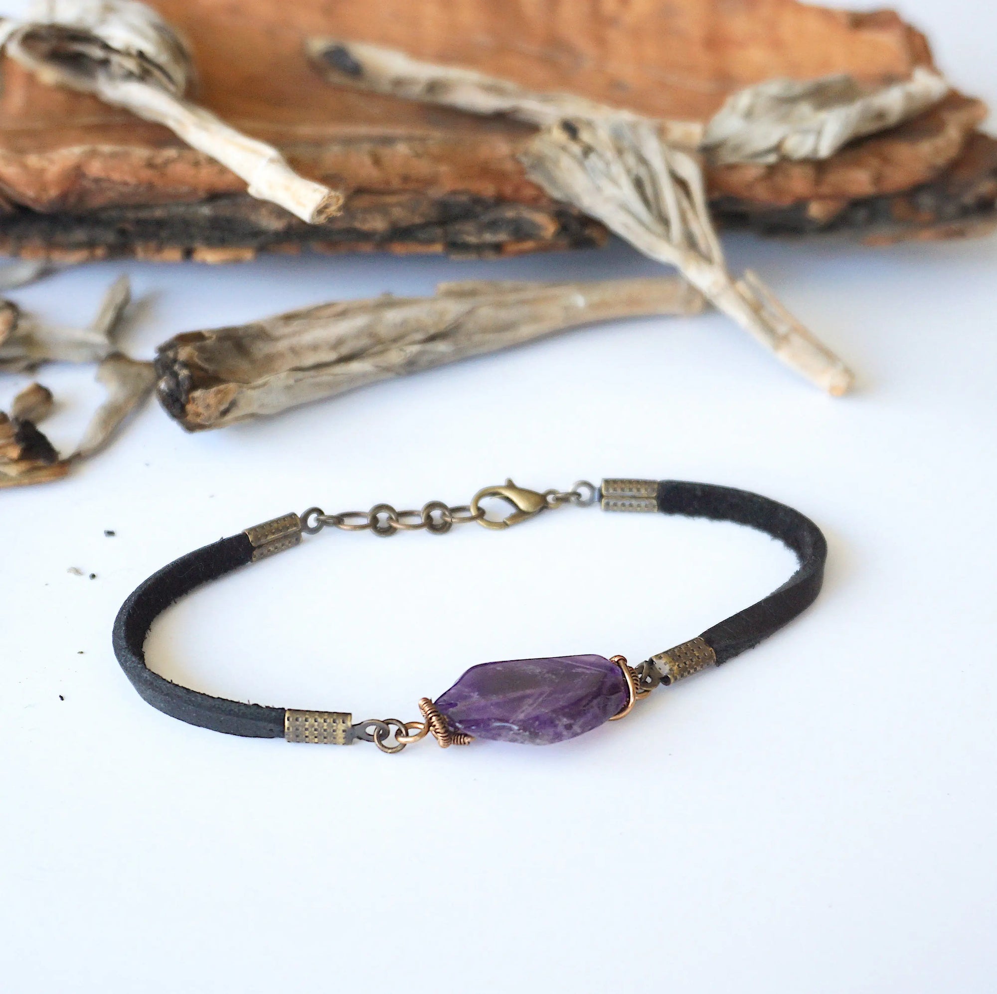 Full view of men’s amethyst bracelet with raw amethyst stone wrapped in antique bronze copper on black leather cord