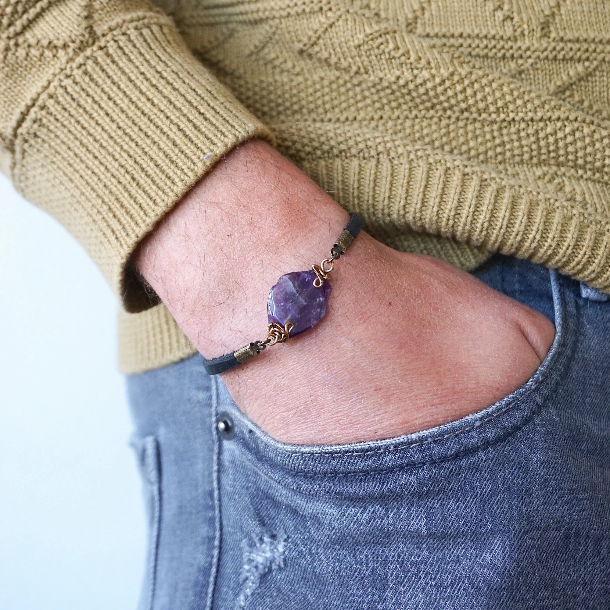 Men’s amethyst bracelet with raw amethyst stone on black leather cord, antique bronze copper wire wrapped, shown on model’s wrist