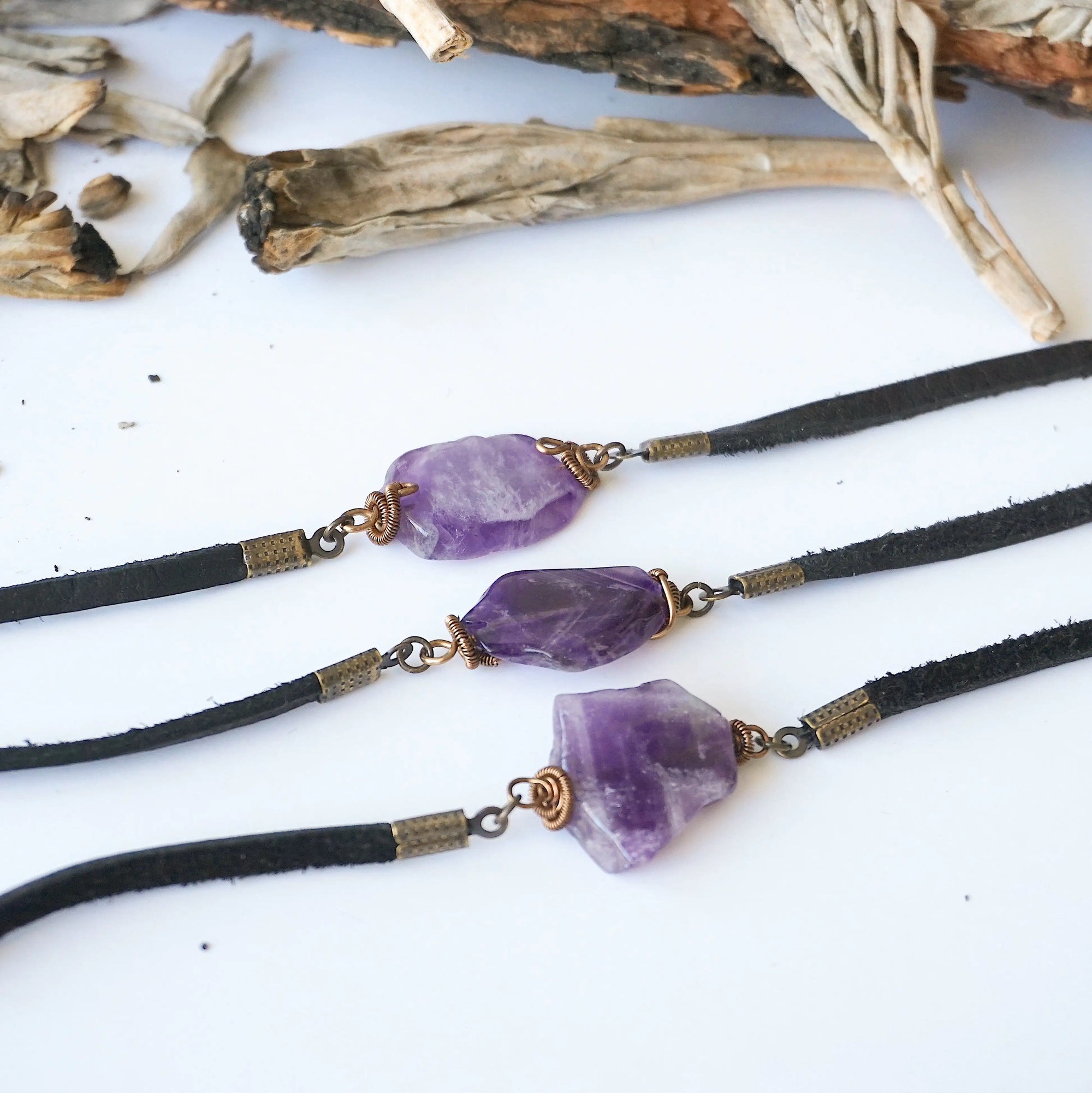 Three men’s amethyst bracelets showing natural variation in amethyst stone color, size, and shape, black leather cord, antique bronze wire wrap