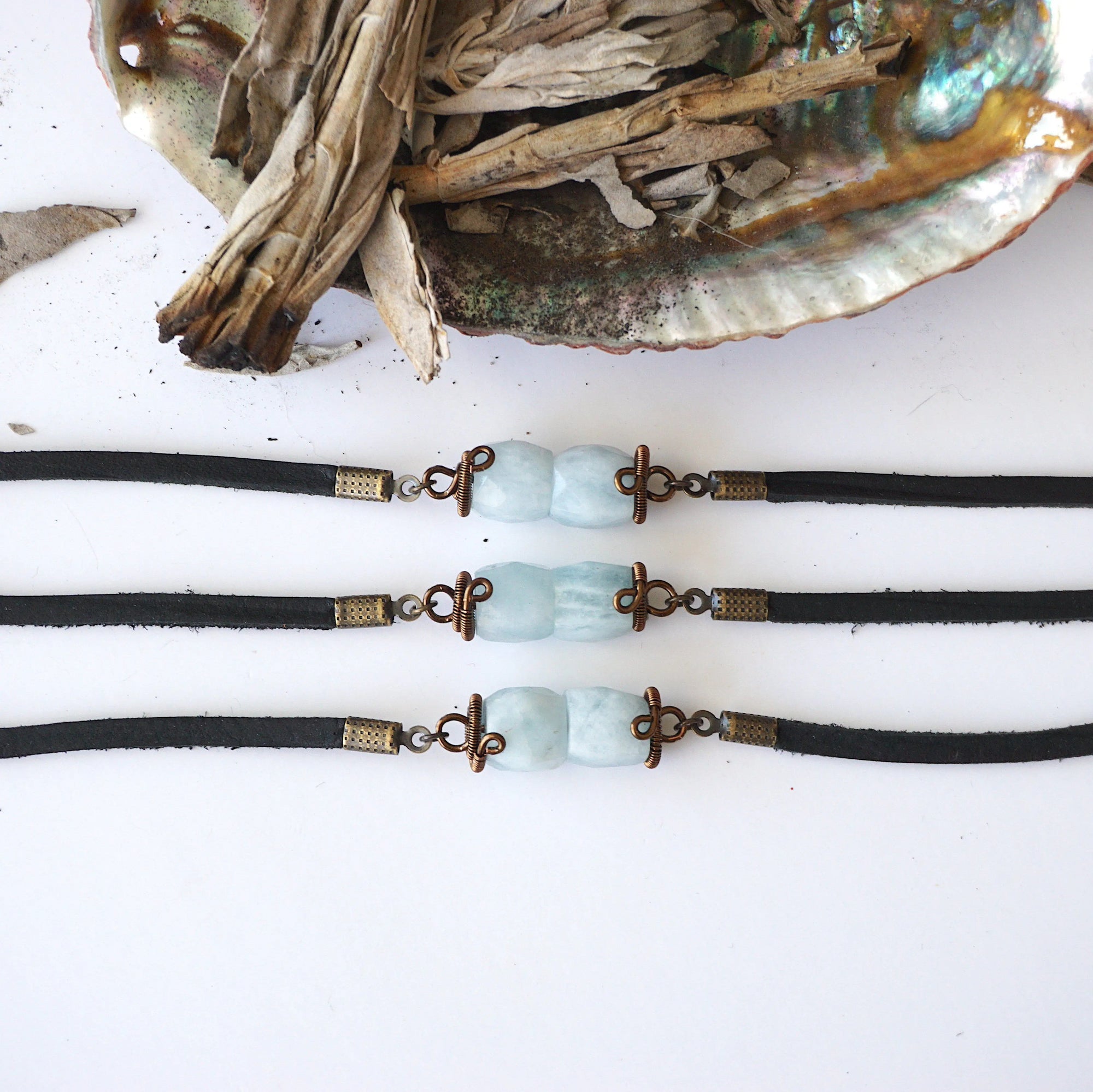 Three men's aquamarine bracelets side by side, showing natural variation in aquamarine color, antique bronze wire, black leather, Designs by Nature Gems