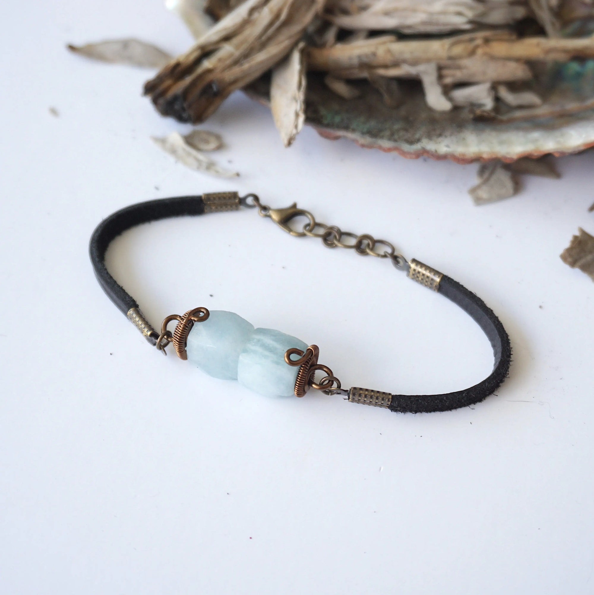 Top view of men's aquamarine bracelet, showing faceted aquamarine stones, antique bronze wire wrapping, and black leather cord