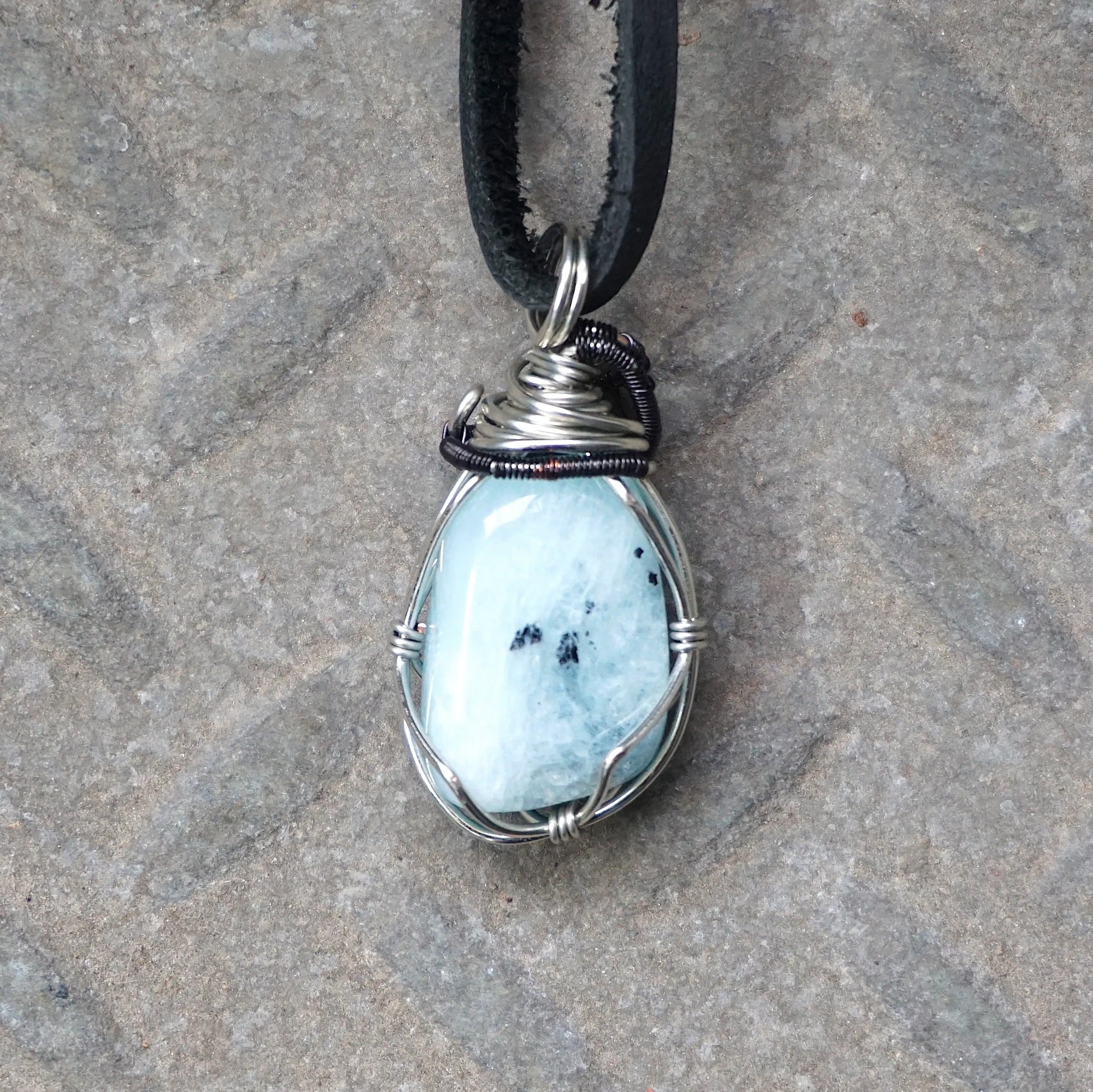 Back angle of men's aquamarine pendant on a black leather cord, highlighting wire wrapped setting and natural stone texture, black and white gold finish