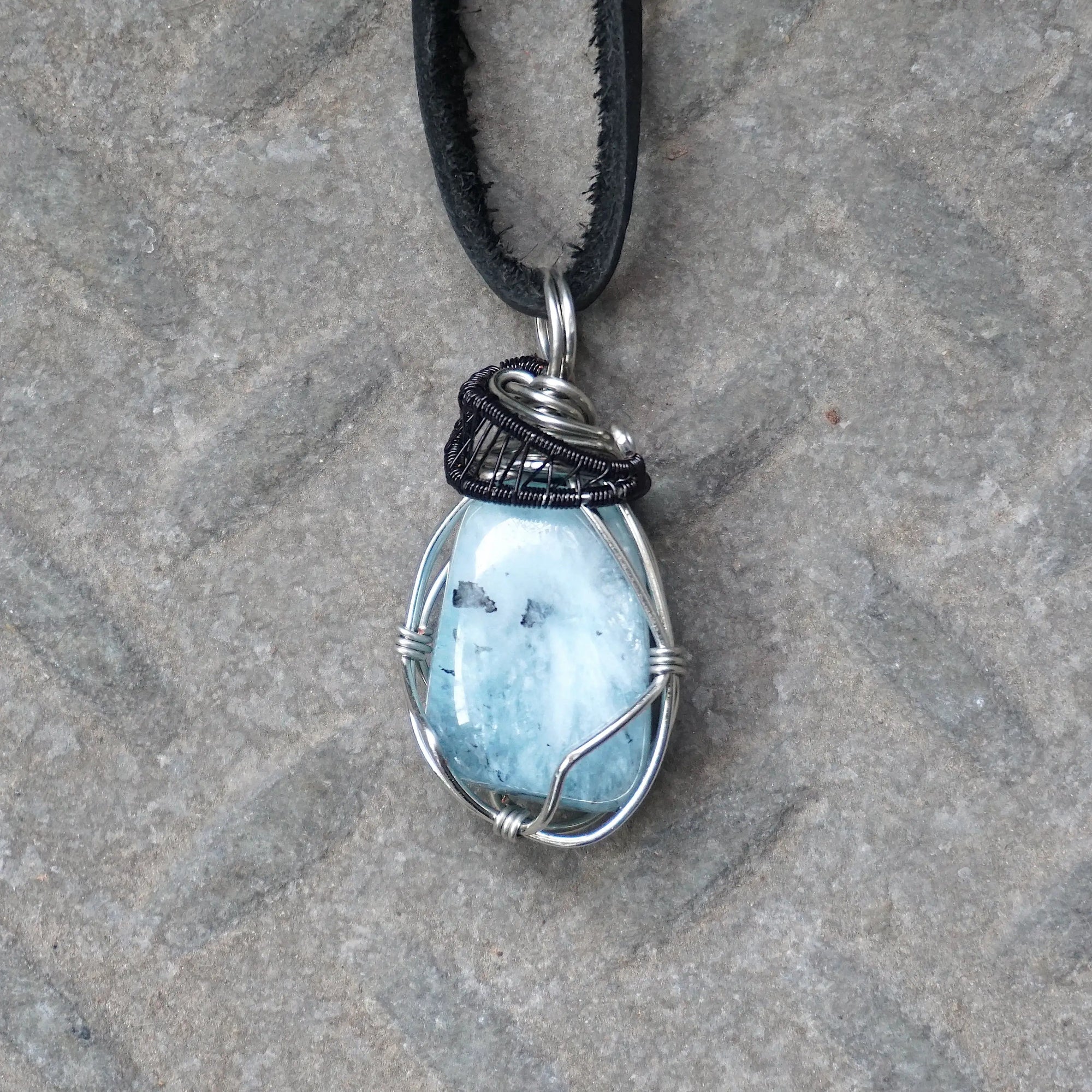 Detailed front angle of men's aquamarine pendant on a black leather cord, artisan wire wrapped in black and white gold finish