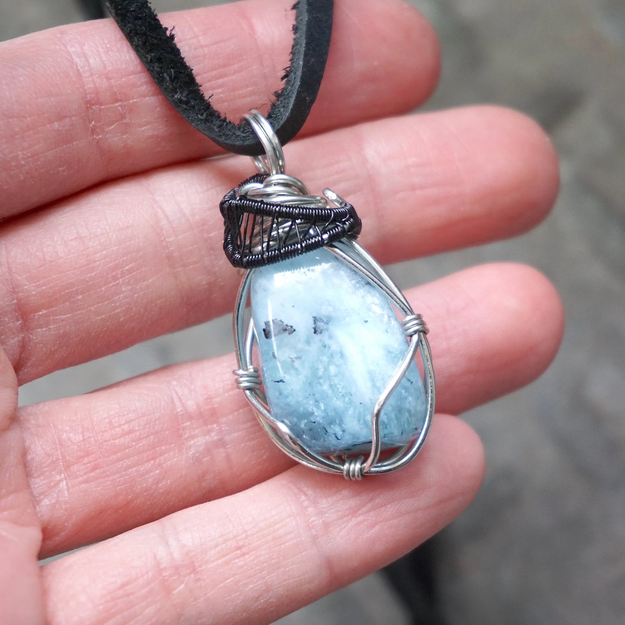 Aquamarine pendant in hand for size reference, genuine polished raw aquamarine, black and white gold finish wire wrapping