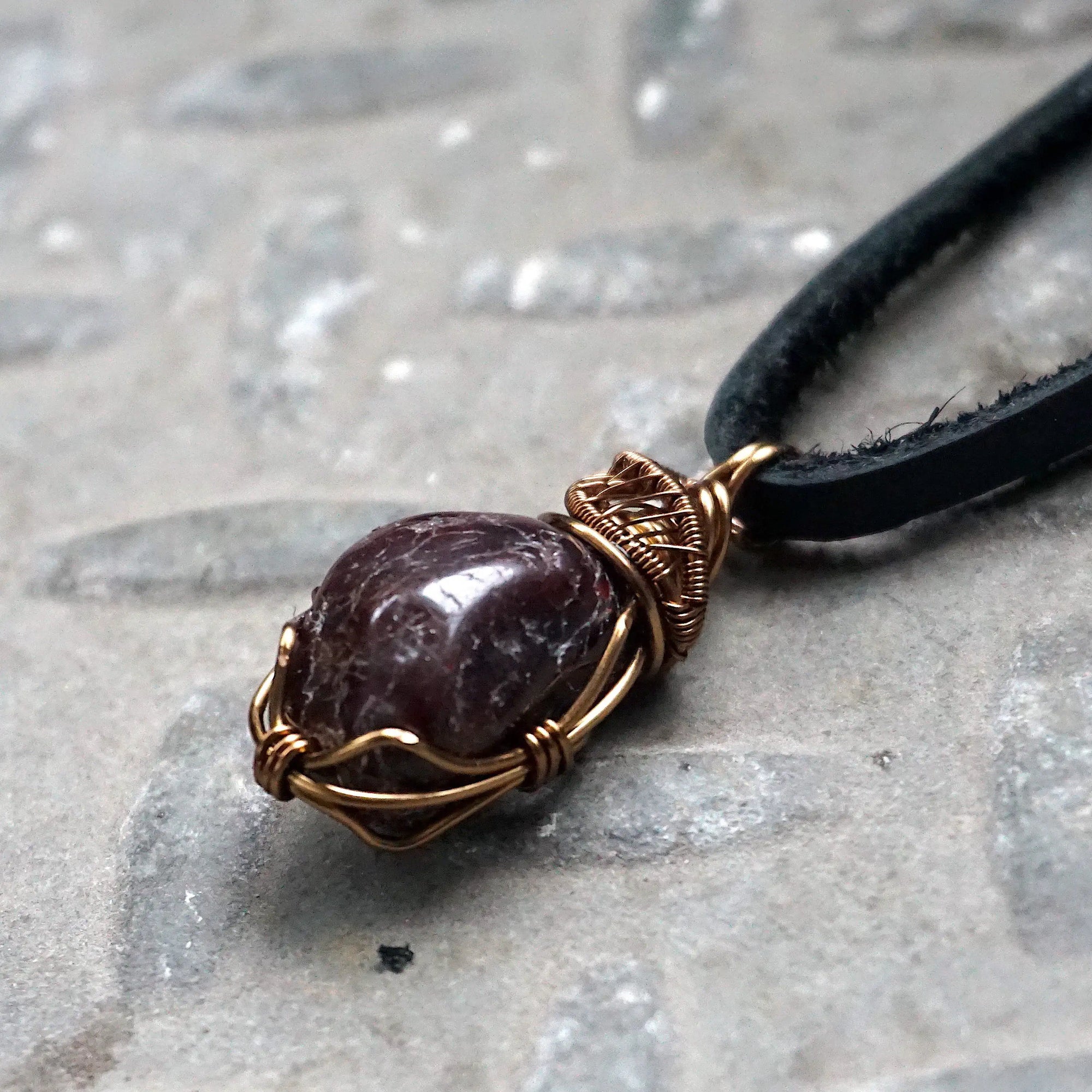 Left side angle view of a men’s garnet wire wrapped necklace, showing the antique bronze copper wrap and natural garnet stone