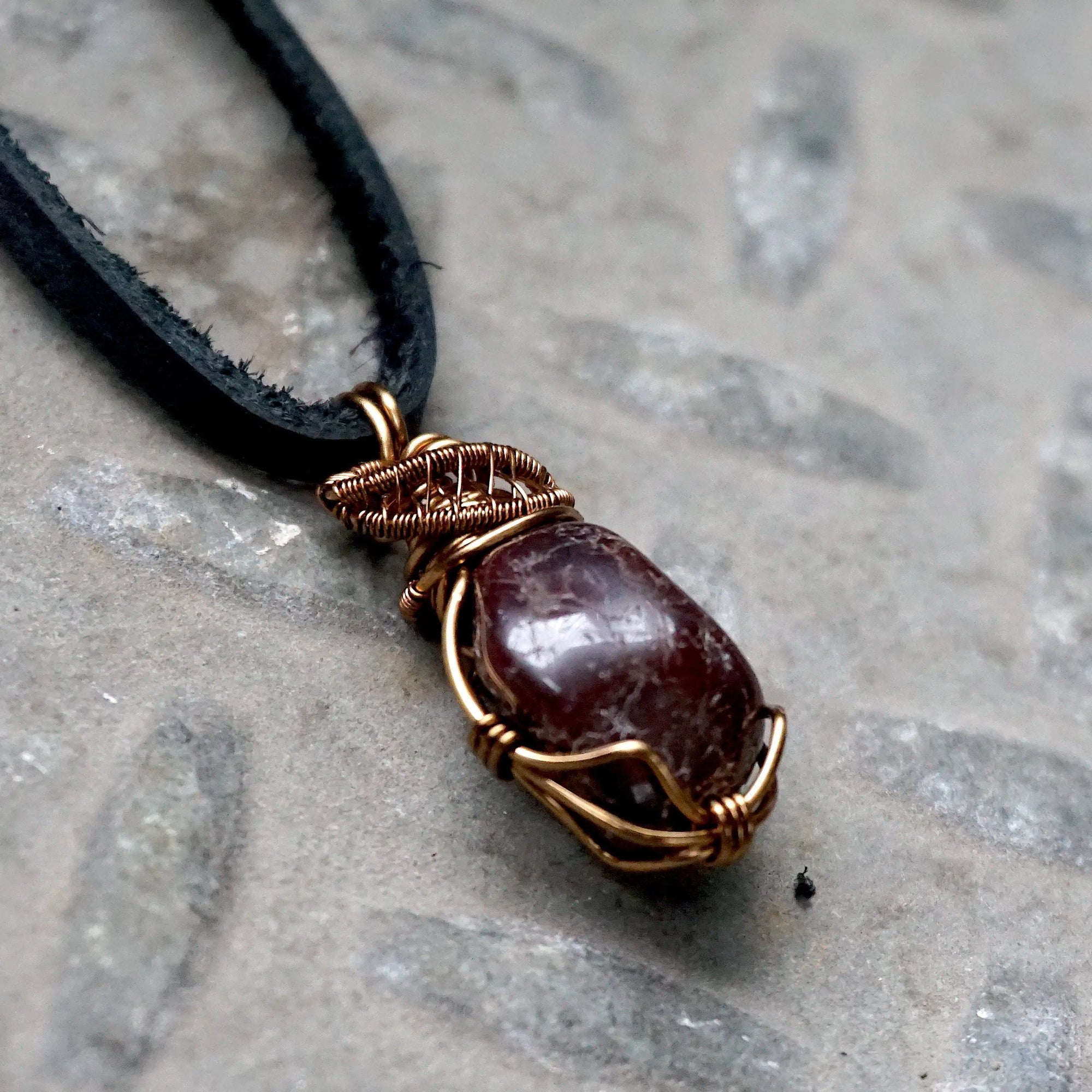 Right side angle view of a men’s garnet wire wrapped pendant in antique bronze copper on a black leather cord