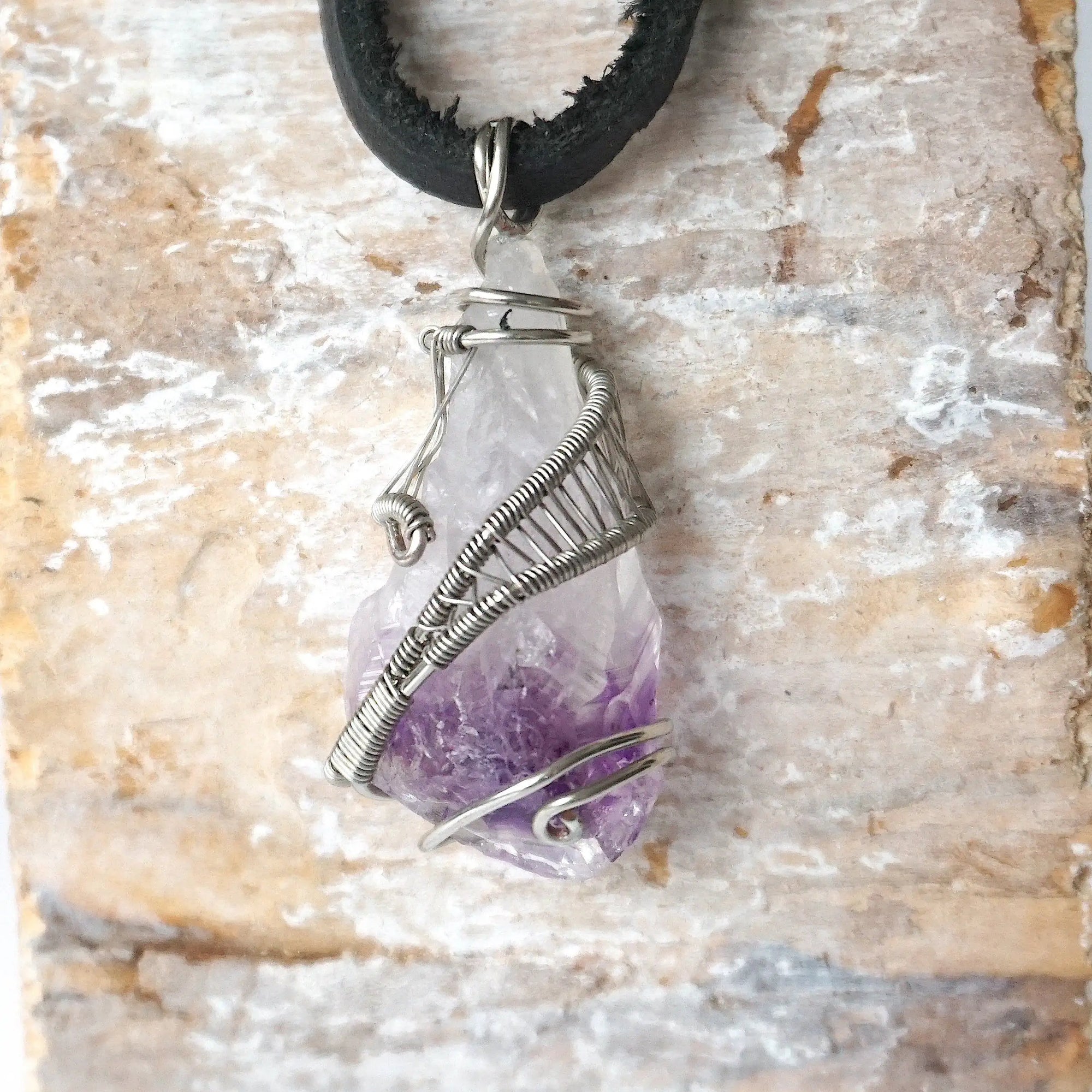 Detailed front view of men’s raw amethyst pendant wire wrapped in white gold plated copper on black leather cord