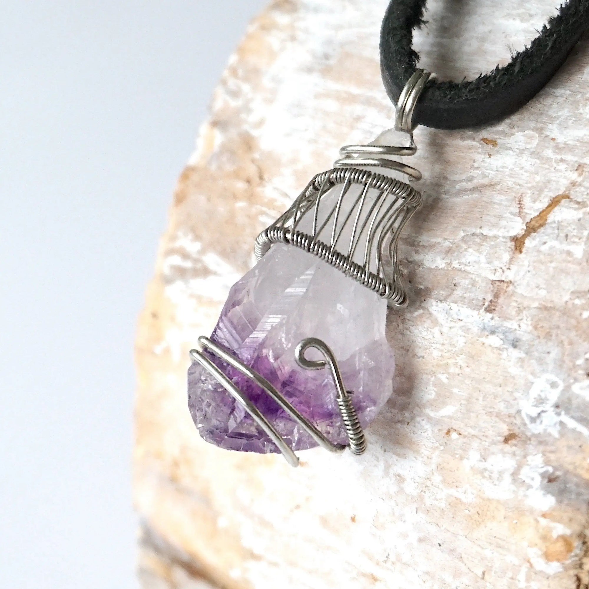 Left side angle of men’s raw amethyst pendant necklace on black leather cord, white gold plated copper wire wrap