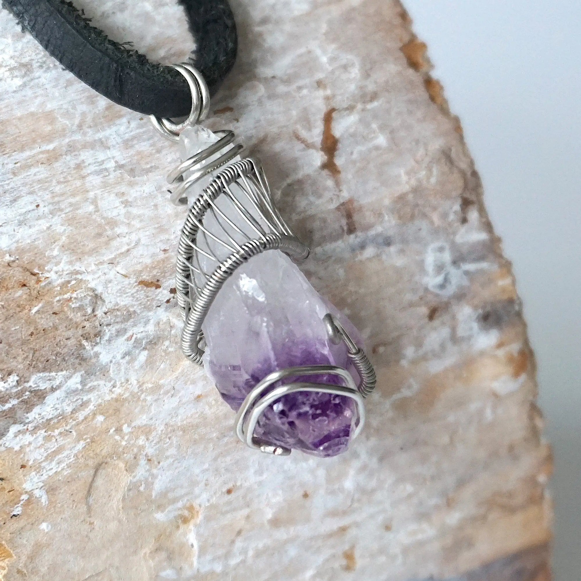 Right side angle of men’s raw amethyst pendant wire wrapped in white gold plated copper on black leather cord