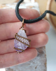 Men’s raw amethyst pendant on black leather cord shown in hand for size reference, antique bronze copper wire wrapped crystal necklace