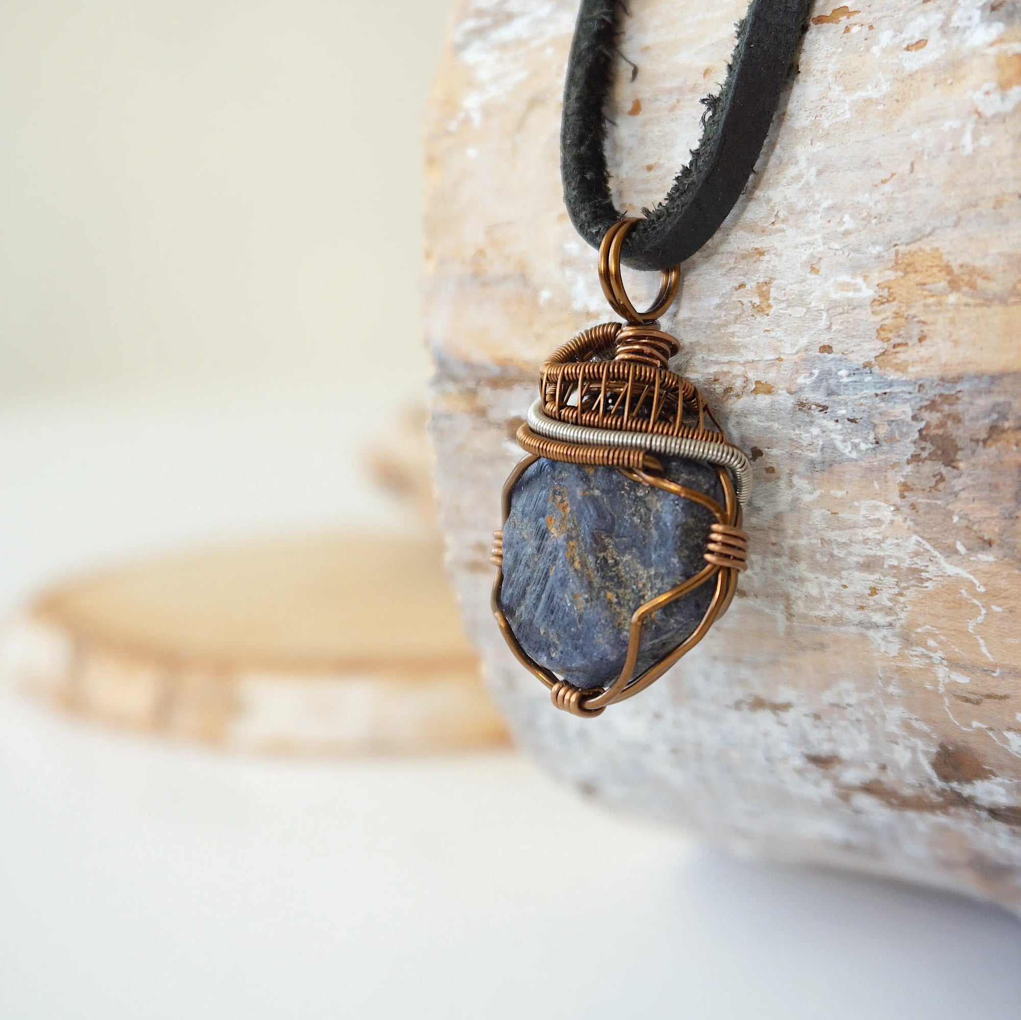 Left-angle close-up of raw sapphire pendant revealing the dual-metal wire-wrapping craftsmanship in antique bronze and dark silver