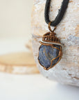 Left-angle close-up of raw sapphire pendant revealing the dual-metal wire-wrapping craftsmanship in antique bronze and dark silver