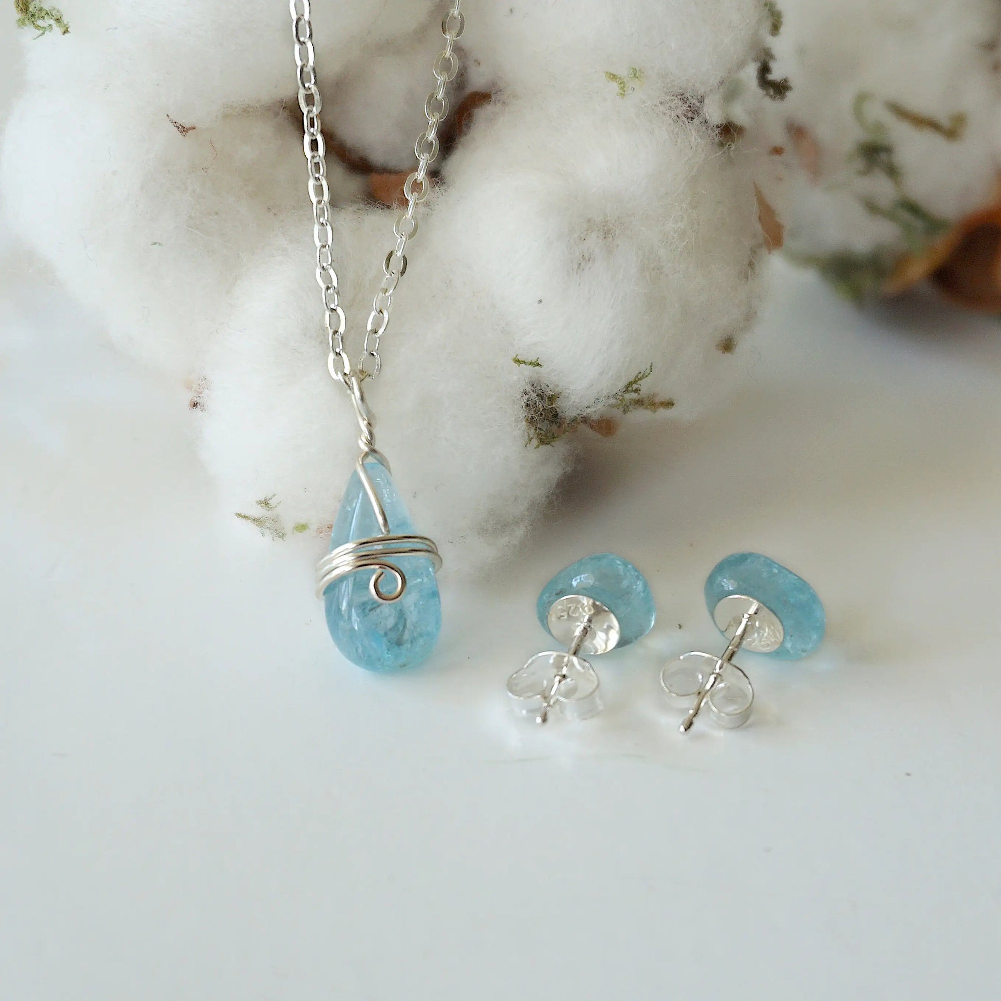 Front angle view of aquamarine necklace and back side of earrings, soft silver wire wrapped pendant and sterling silver stud earrings, March birthstone