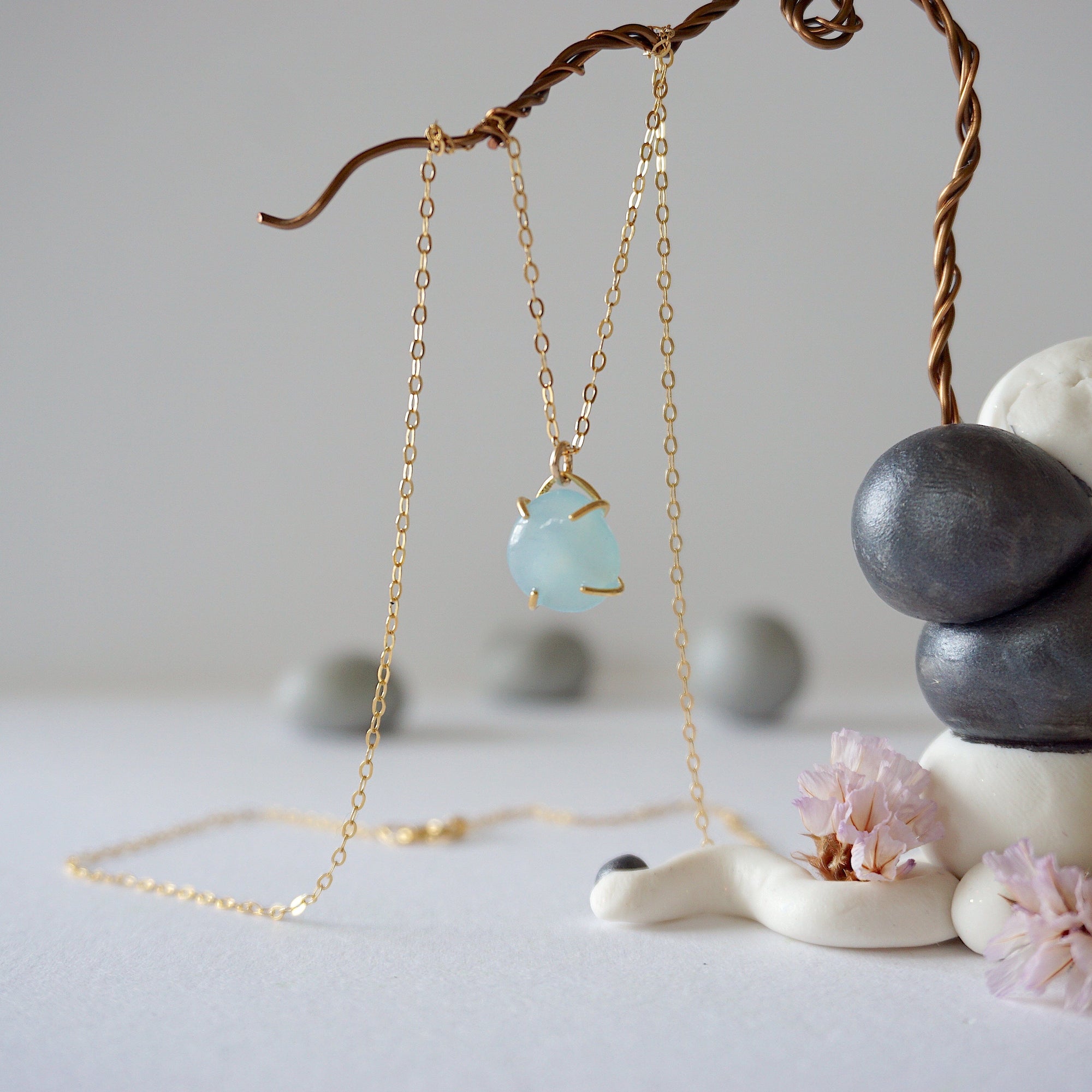 Zoomed out view of minimalist aquamarine necklace in gold, hanging on display, artisan claw setting, gold filled chain