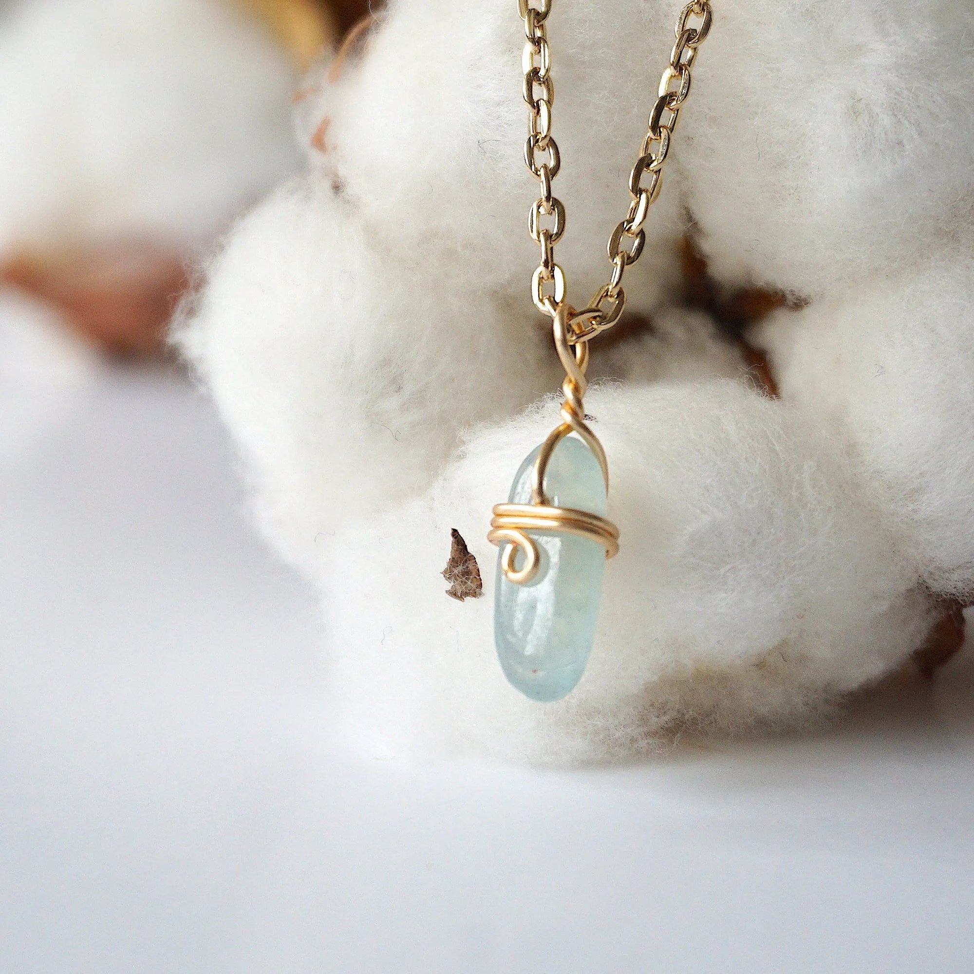 Left side angle of minimalist aquamarine necklace, polished aquamarine pendant, warm gold wire wrapping