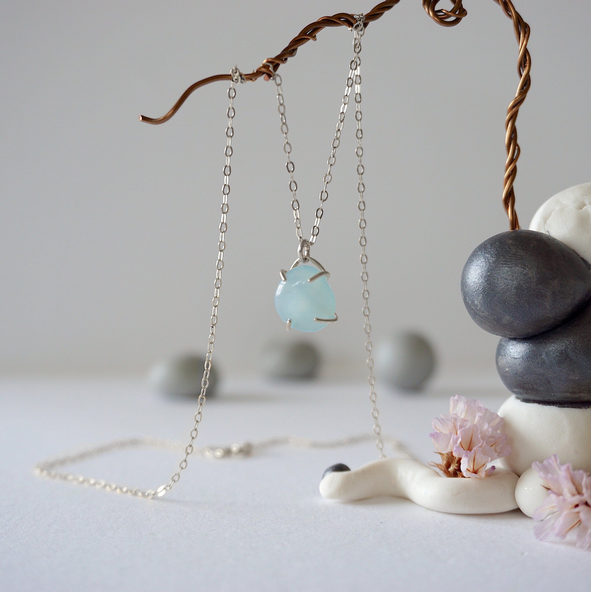 Zoomed out view of minimalist aquamarine necklace hanging on display, artisan claw setting, sterling silver chain