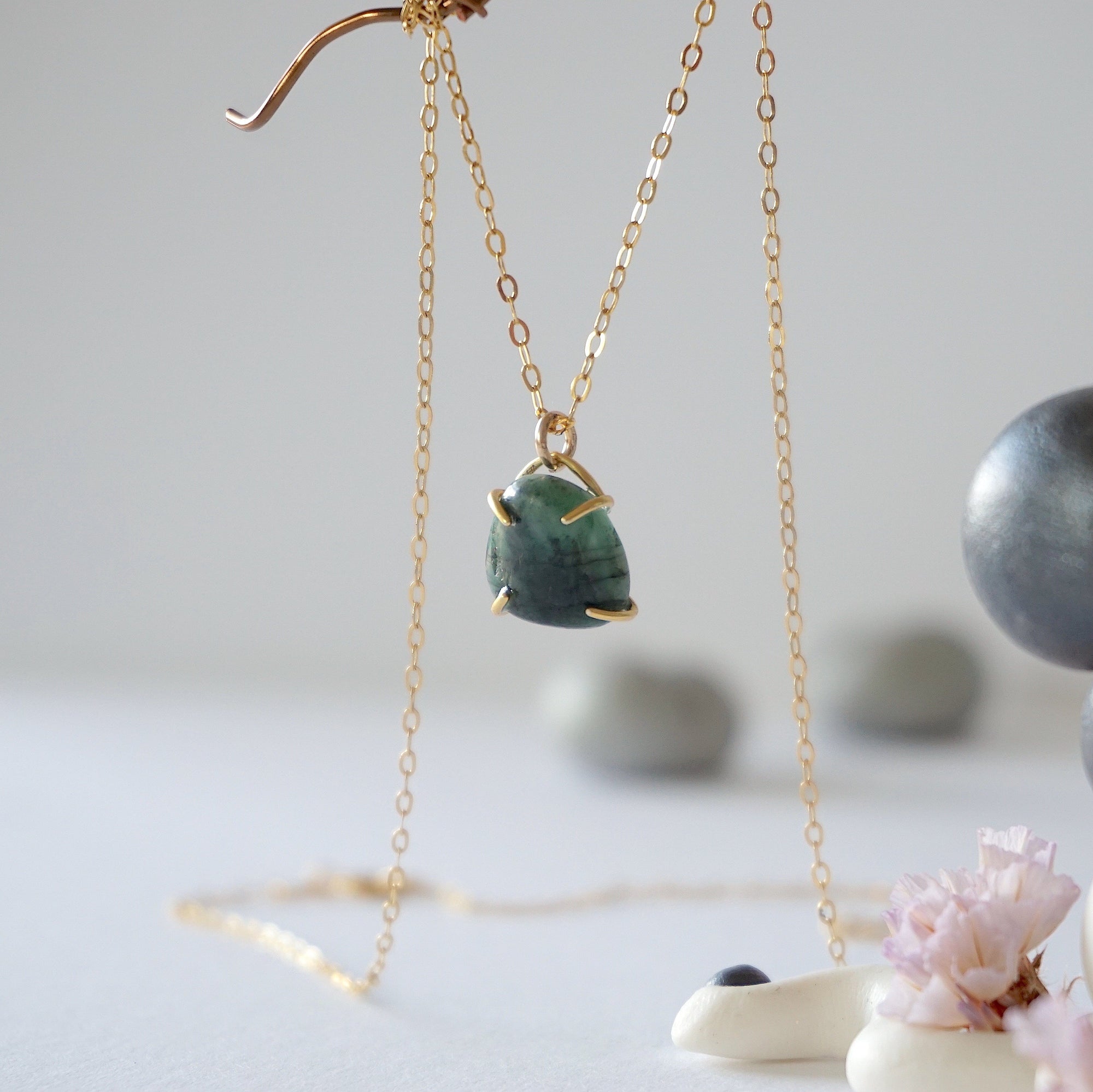 Side angle view of minimalist emerald necklace showing gold vermeil prong setting and natural raw emerald.