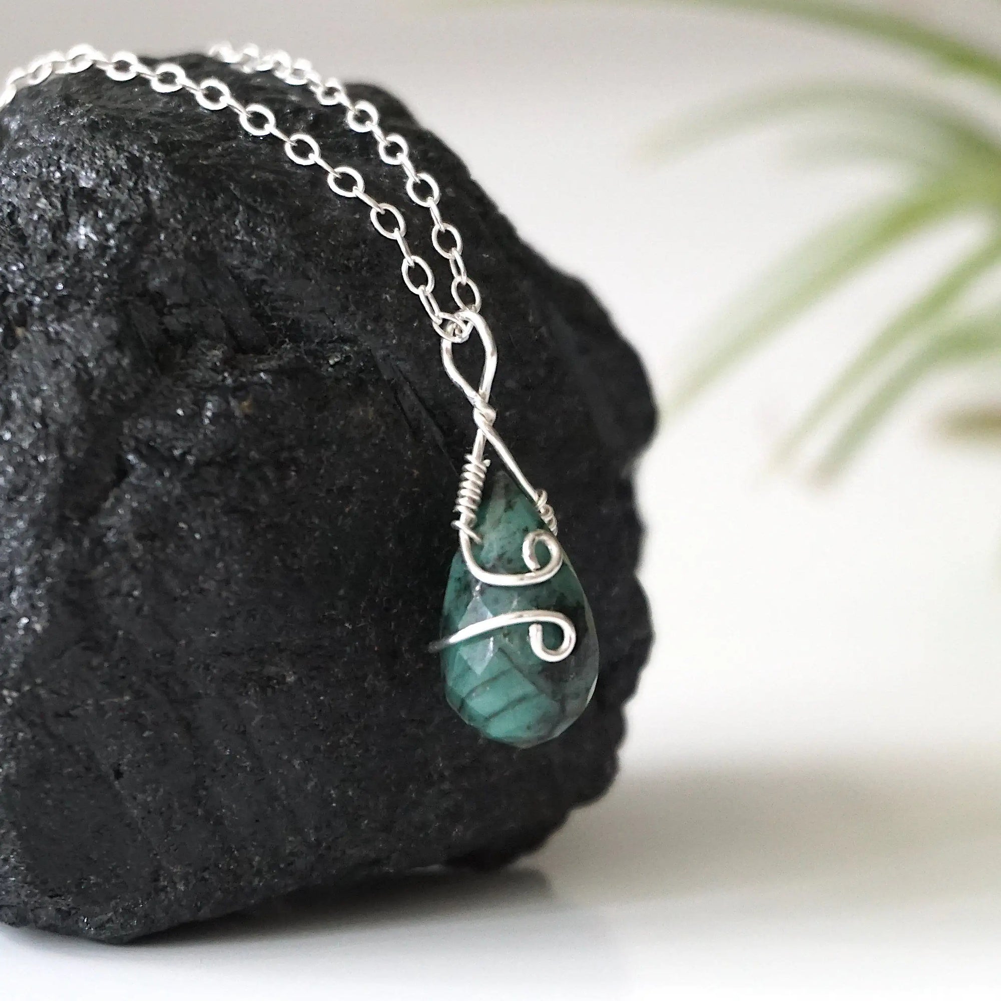 Right angle detail of minimalist emerald pendant for women with natural faceted teardrop emerald and sterling silver wrapping