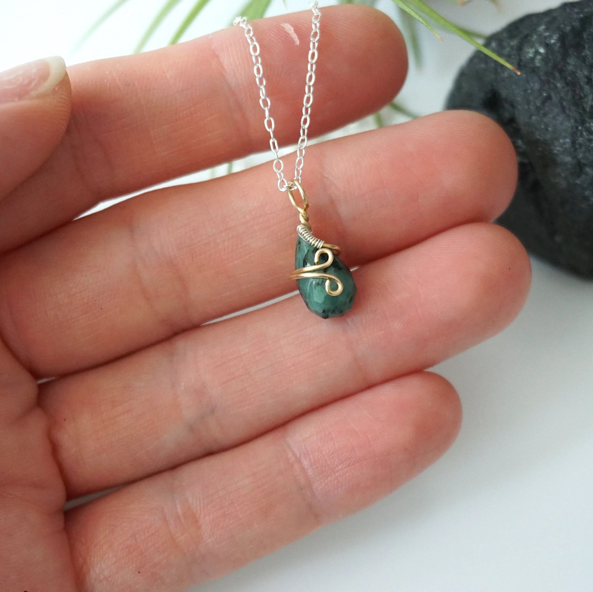 Minimalist emerald necklace for women shown in hand for size reference with natural faceted emerald and mixed metal wire wrapping