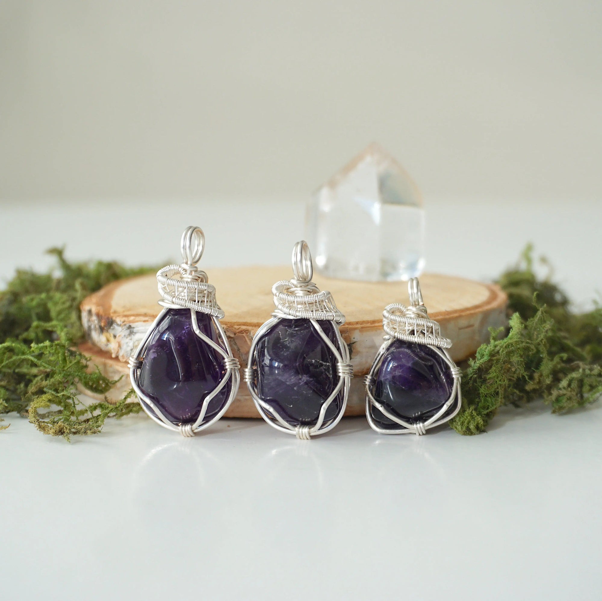Three natural amethyst pendants showing variation in stone color, size, and shape, handmade wire wrapped jewelry