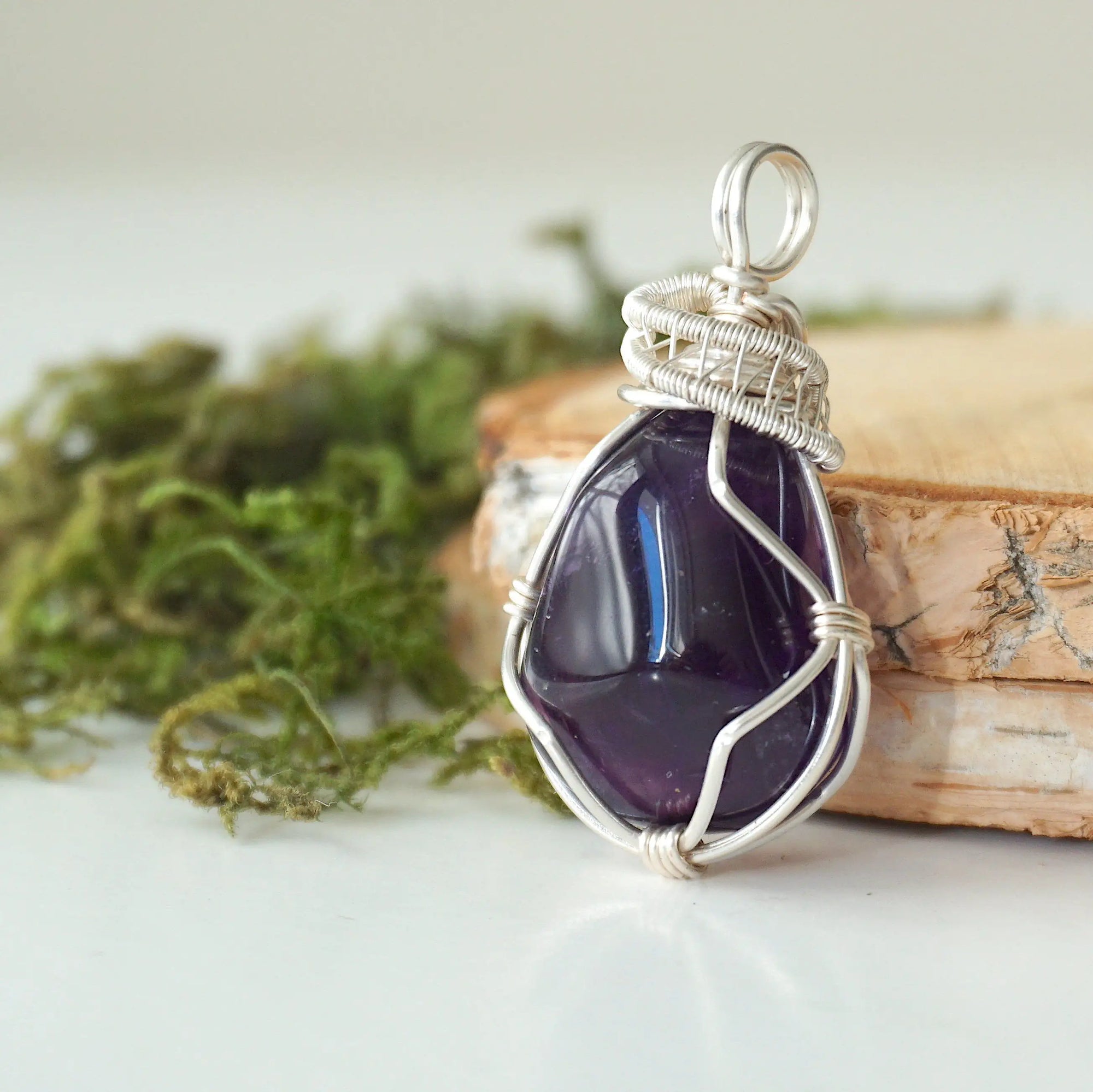 Side view detail of polished dark amethyst pendant with sterling silver wire wrapping, handmade necklace