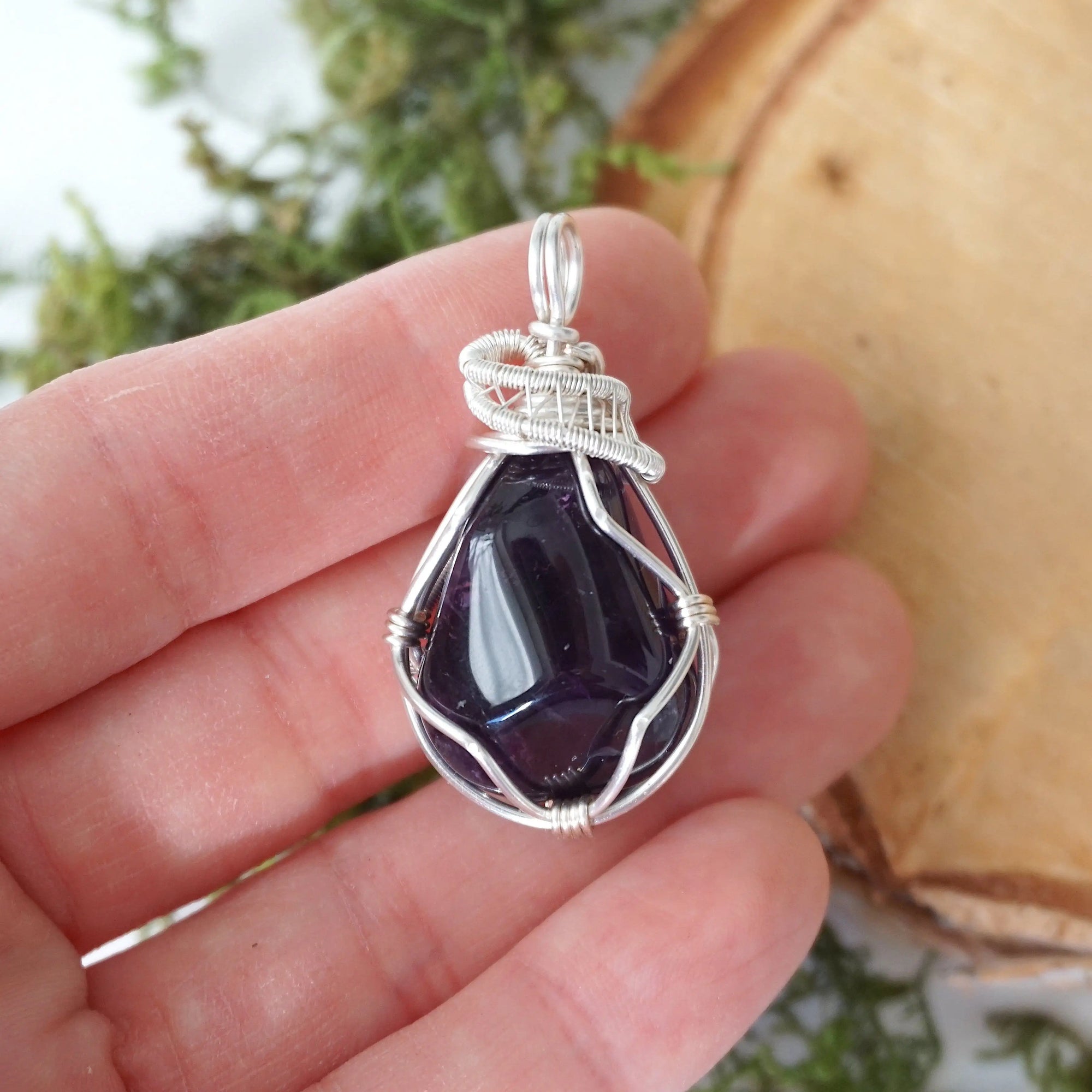 Natural dark amethyst pendant held in hand for size reference, handmade sterling silver wire wrapped necklace