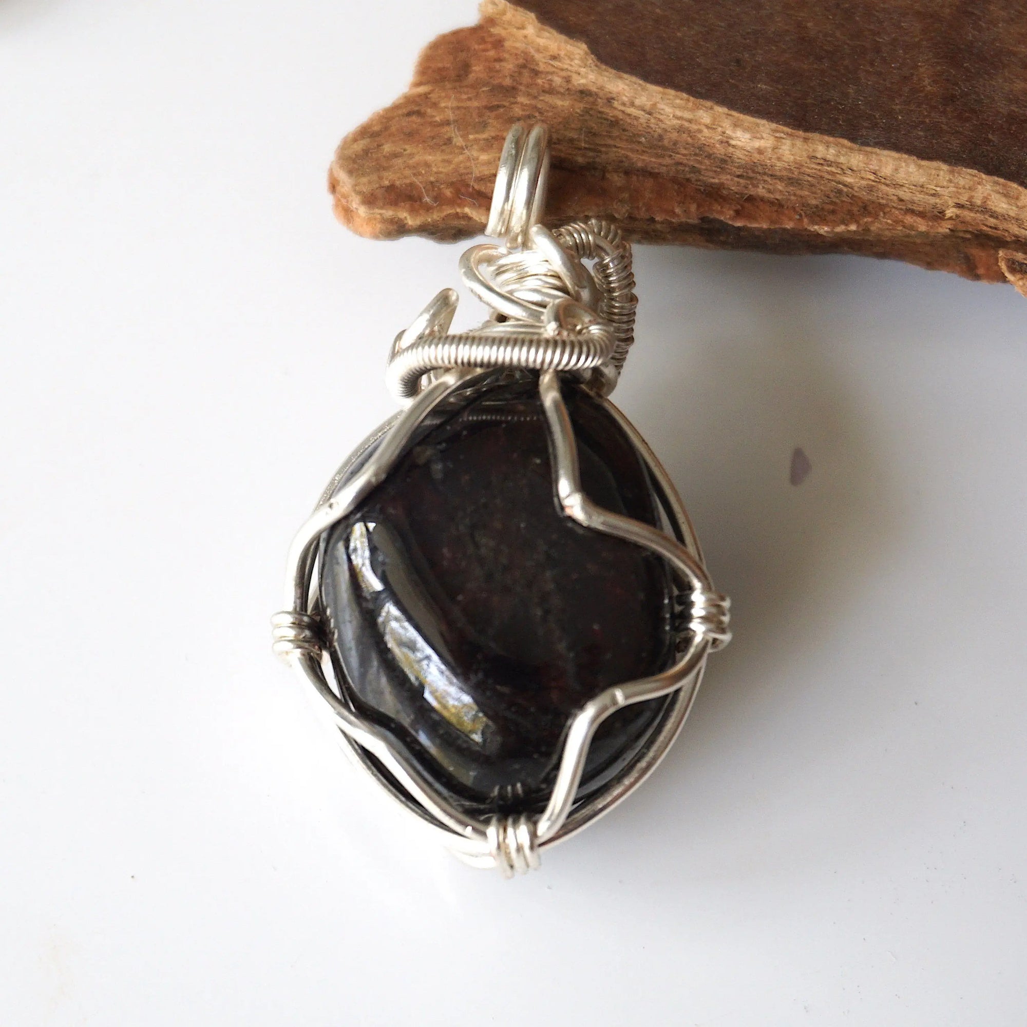 Back view of raw garnet pendant highlighting intricate silver plated copper wire wrap craftsmanship
