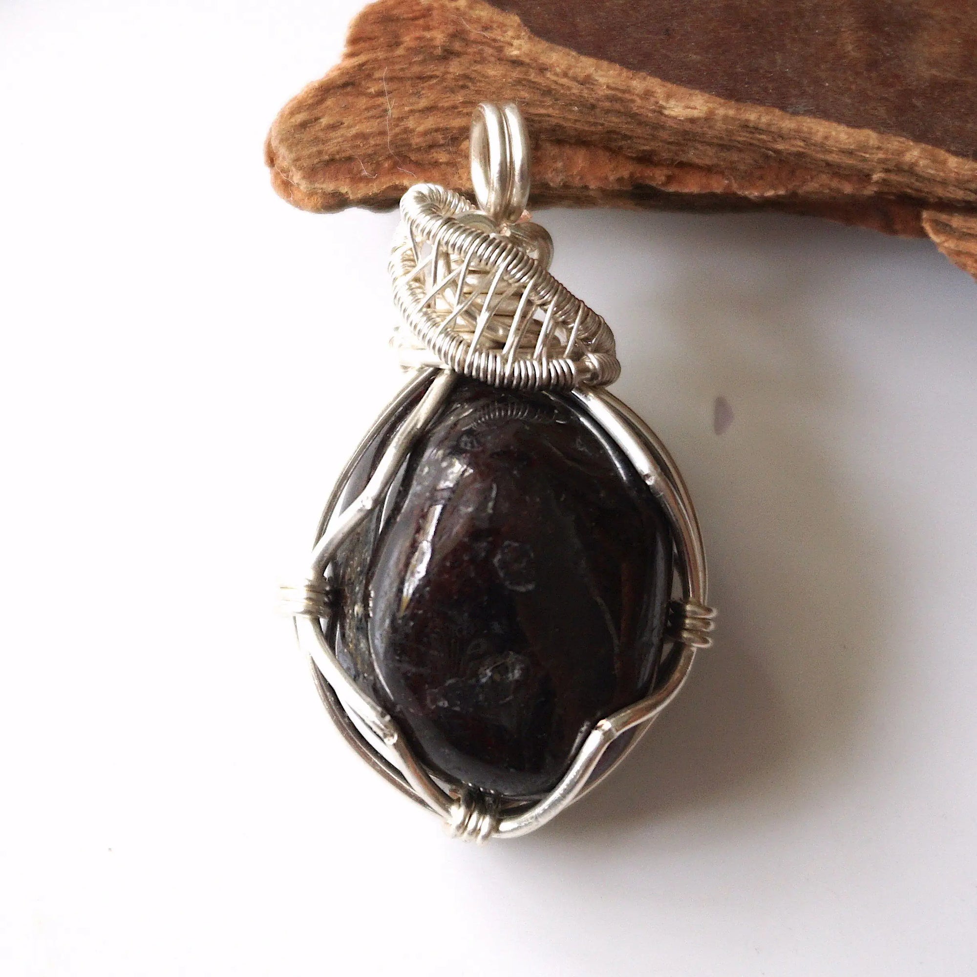 Detailed front view of natural raw garnet pendant with intricate silver plated copper wire wrapping