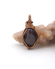 Detailed front angle of handmade raw garnet crystal pendant wire wrapped in antique bronze copper